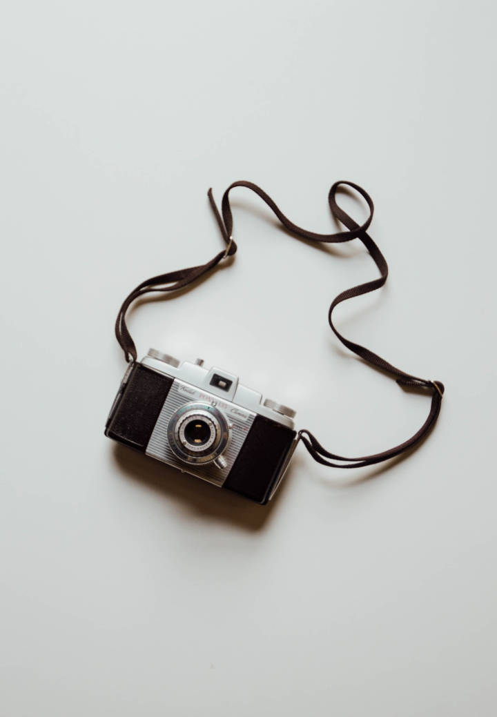 Vintage Minimalist 桌布 壁紙 — 一部帶有棕色背帶的復古銀黑底片相機，放置在純白色表面上。