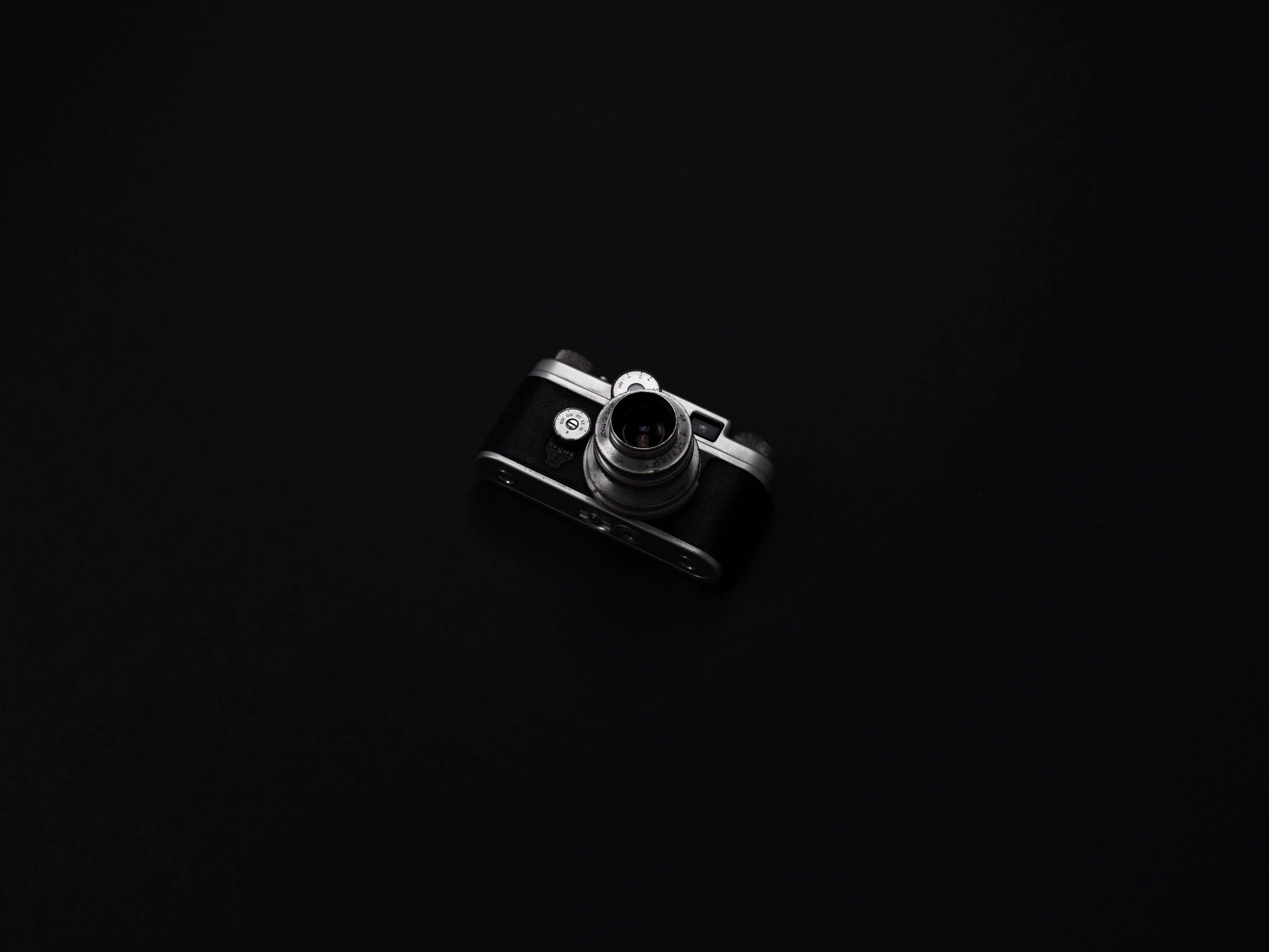 Dslr 桌布 壁紙 — 一部帶有銀色裝飾的復古相機，在柔和的方向性燈光下，居中放置在深黑色背景上。