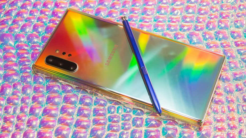 Note 10 桌布 壁紙 — 一部彩虹色的三星手機連藍色觸控筆放在粉紅色泡泡糖虹彩表面上。