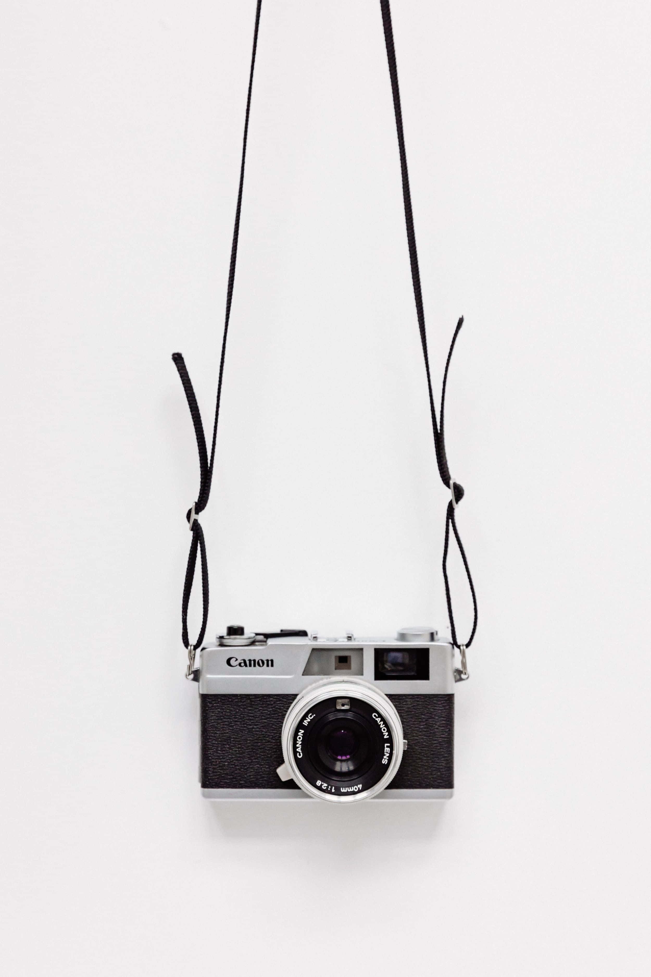 Minimalist Photography 桌布 壁紙 — 一部復古 Canon 底片相機用黑色掛帶掛在純白背景上。