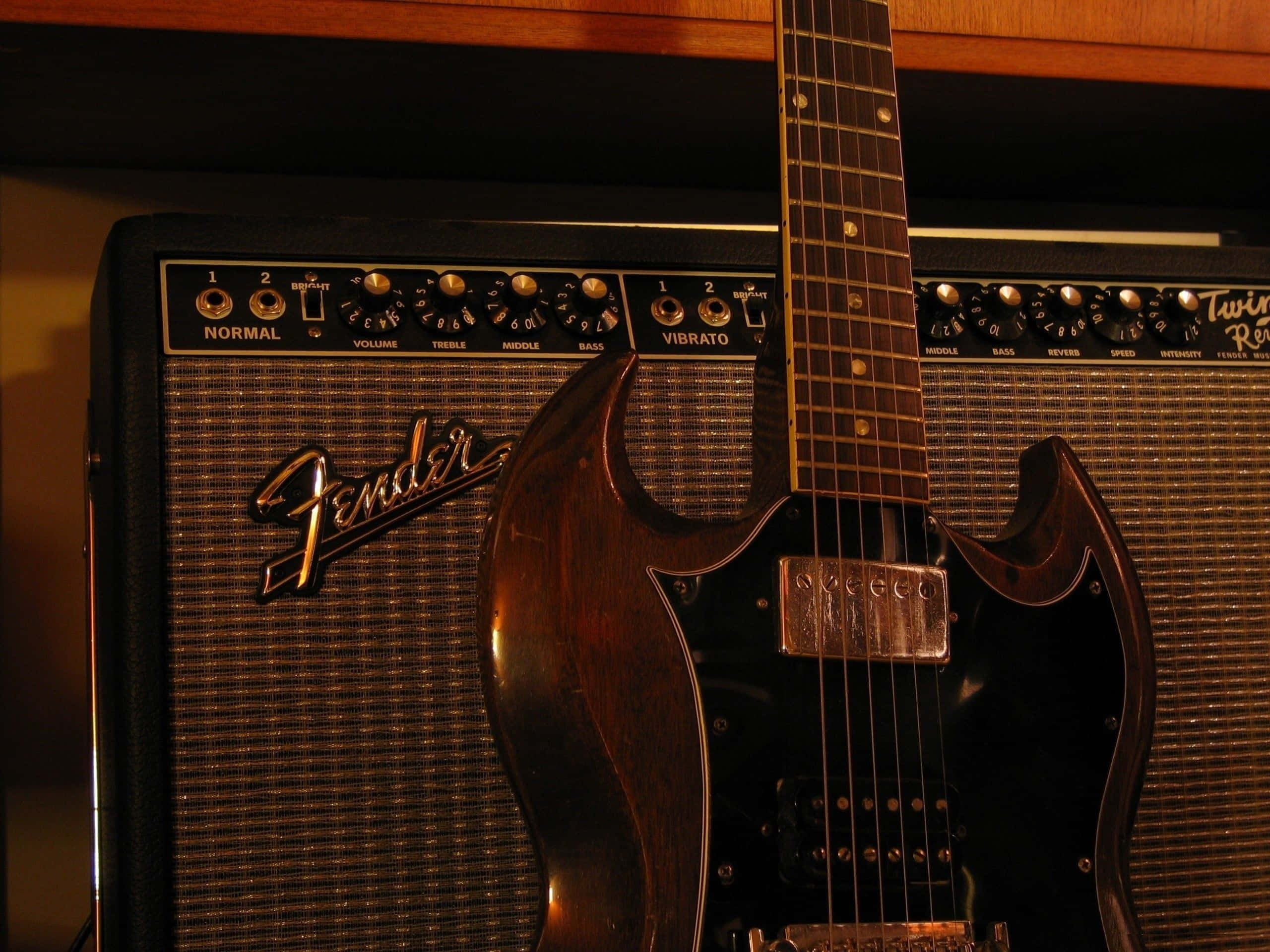 Guitar Amp 桌布 壁紙 — 一部復古 Fender Twin Reverb 擴音器，旁邊有一把深色木吉他靠在上面，在溫暖的環境燈光下。