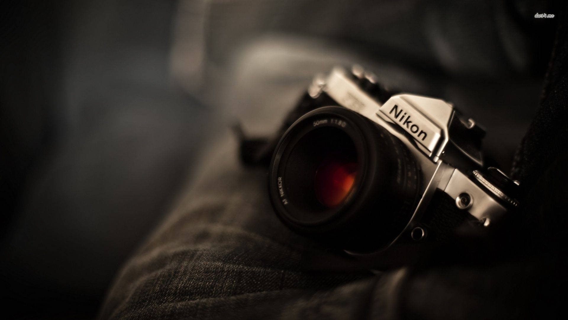 攝影 桌布 壁紙 — 一部復古 Nikon 底片相機放置在牛仔布上，景深淺，鏡頭帶有溫暖光暈。