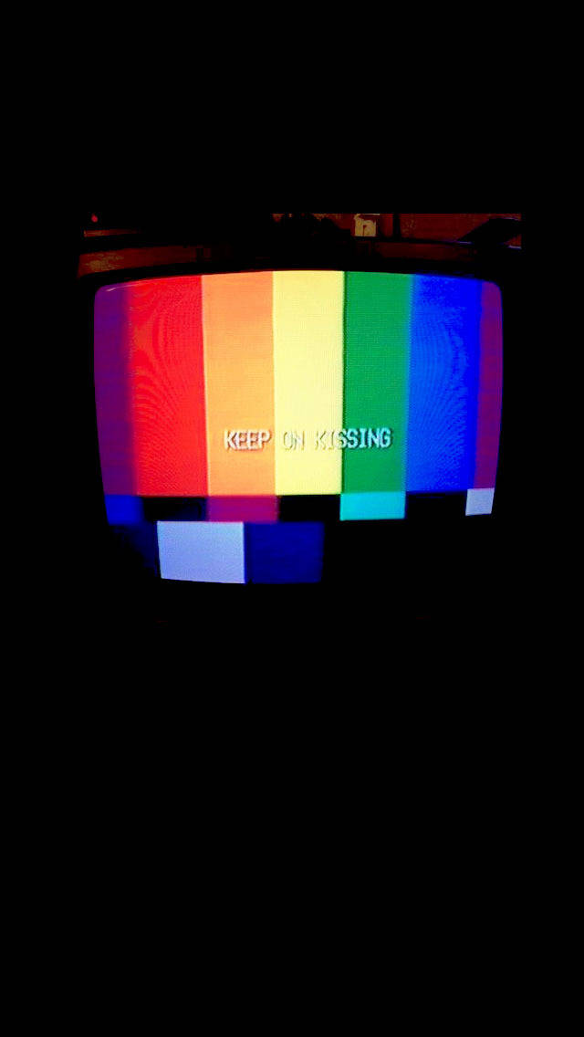桌布 壁紙 — 一部復古CRT電視顯示彩色測試圖案，文字「keep on kissing」在黑暗環境中發出白色光芒。