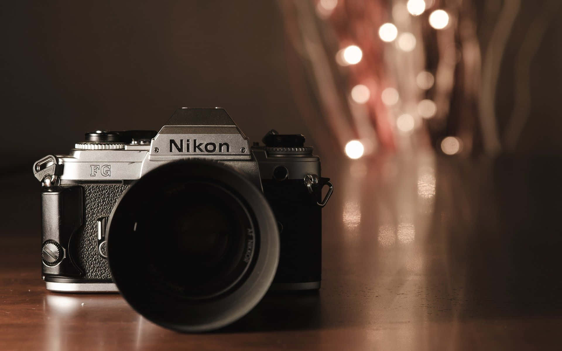 攝影 桌布 壁紙 — 一部復古Nikon FG底片相機放在木質表面上，背景有溫暖的散景燈光柔和地發光。