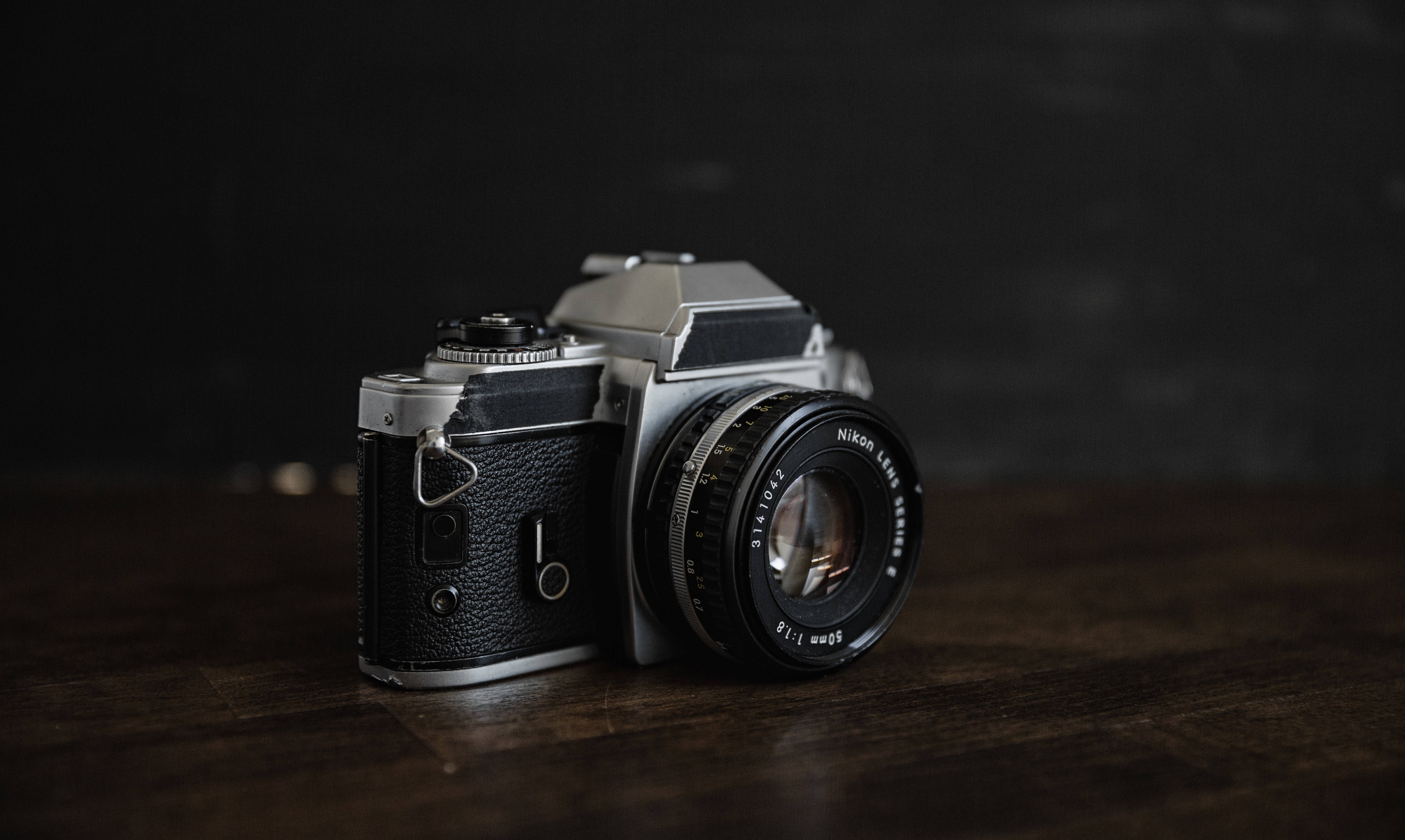 Vintage Minimalist 桌布 壁紙 — 一部復古Nikon底片相機放置在深色木質表面上，背景為黑色，光線柔和。