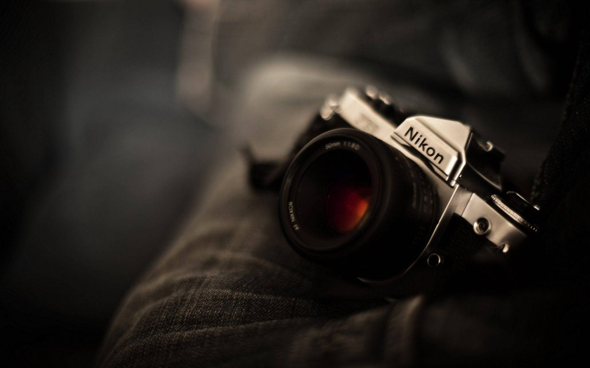 相機 桌布 壁紙 — 一部復古Nikon底片相機放置在深色牛仔布上，景深淺，帶有溫暖的電影感燈光。