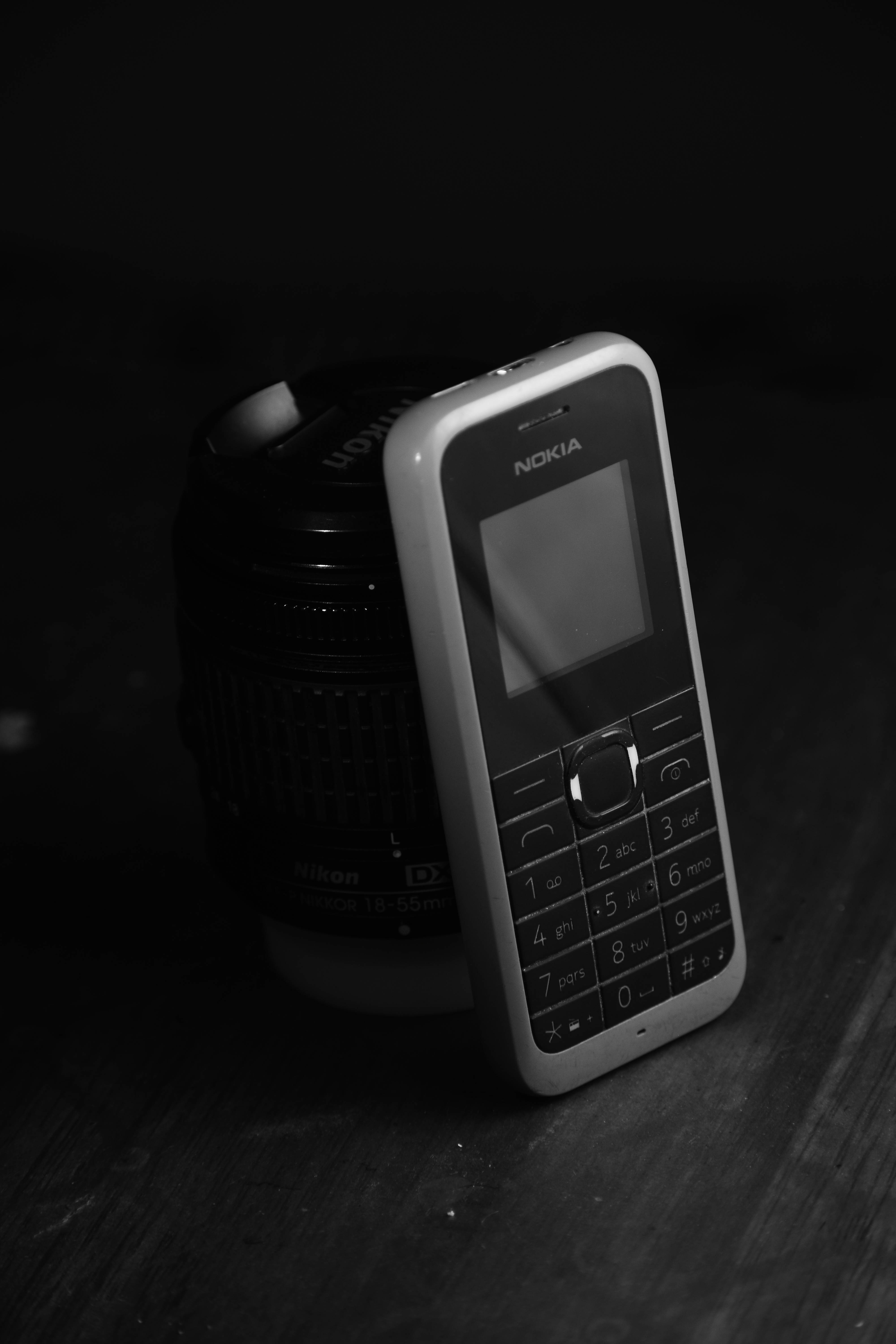 諾基亞 桌布 壁紙 — 一部復古Nokia手機靠著Nikon鏡頭，置於深色木質表面上，呈單色調。