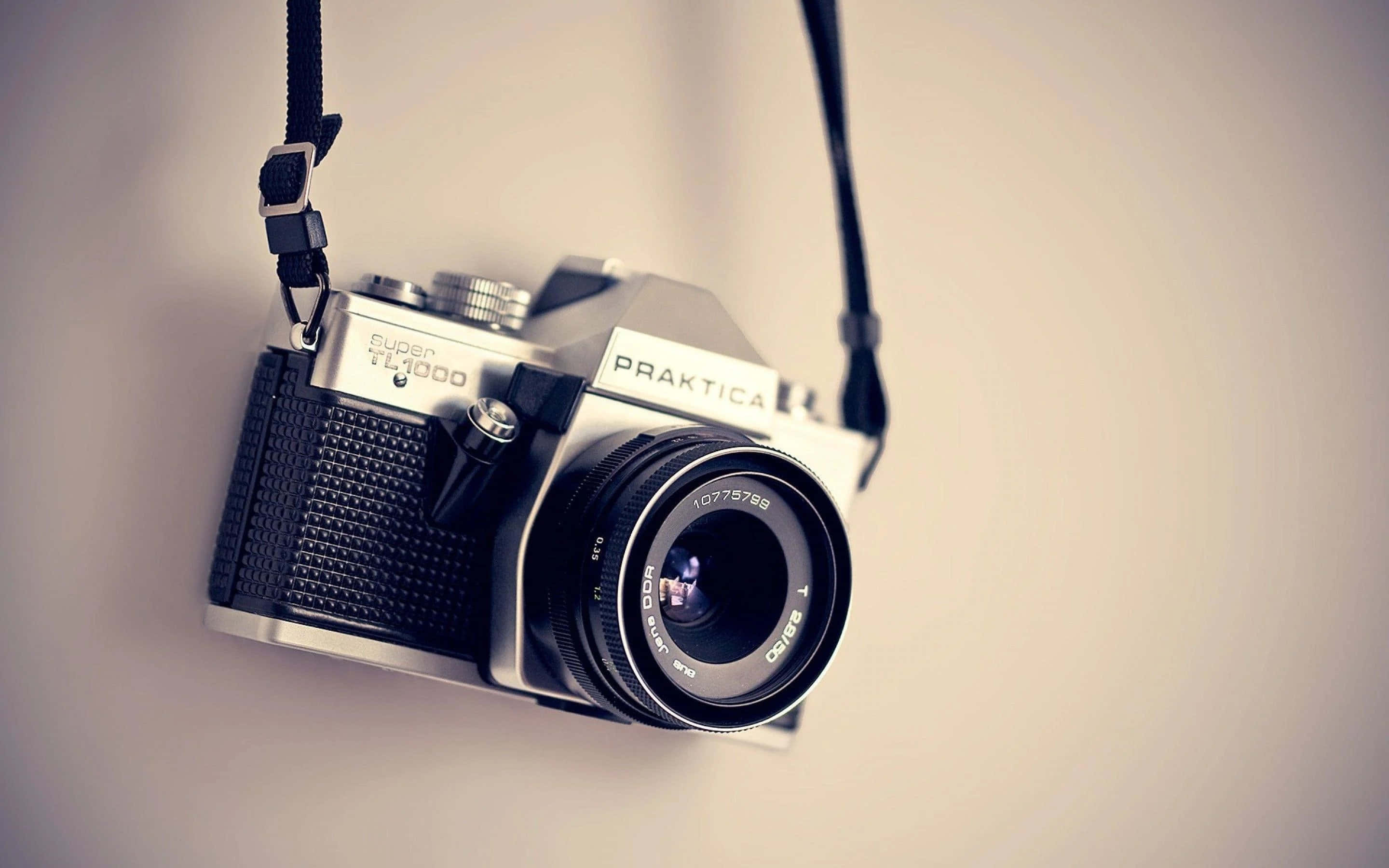 相機 桌布 壁紙 — 一部復古Praktica TL1000底片相機用掛帶懸掛在柔和的米色牆上。