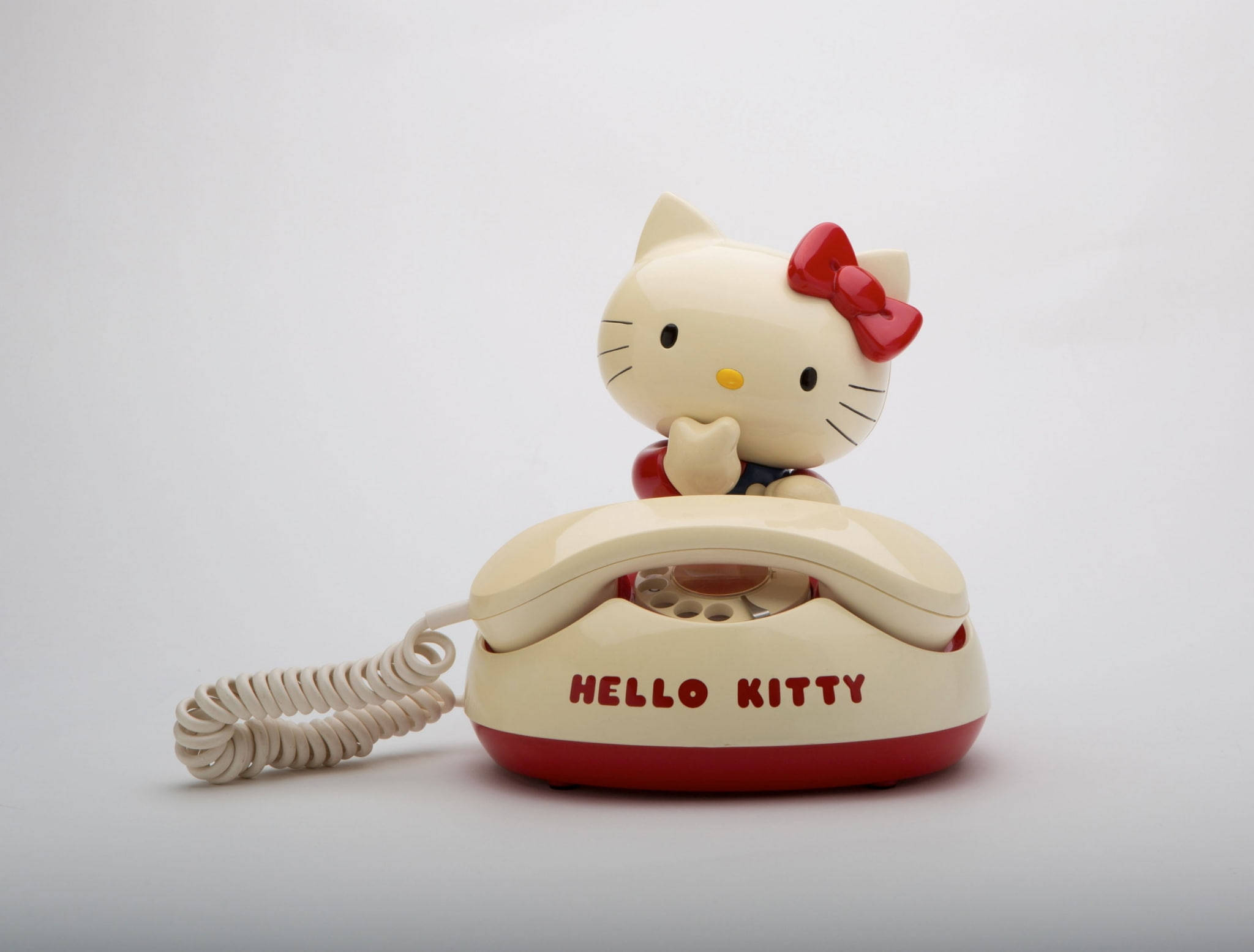 Hello 桌布 壁紙 — 一部復古奶油色和紅色的Hello Kitty旋轉電話，角色棲息在頂部，背景為純白色。