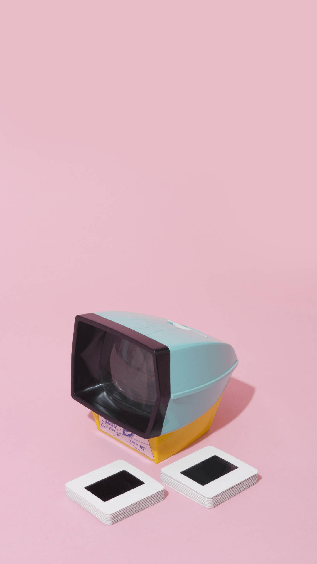 Aesthetic Retro 桌布 壁紙 — 一部復古幻燈機，帶有青綠色和黃色點綴，放置在柔和的粉紅色背景上，旁邊有兩疊空白幻燈片。