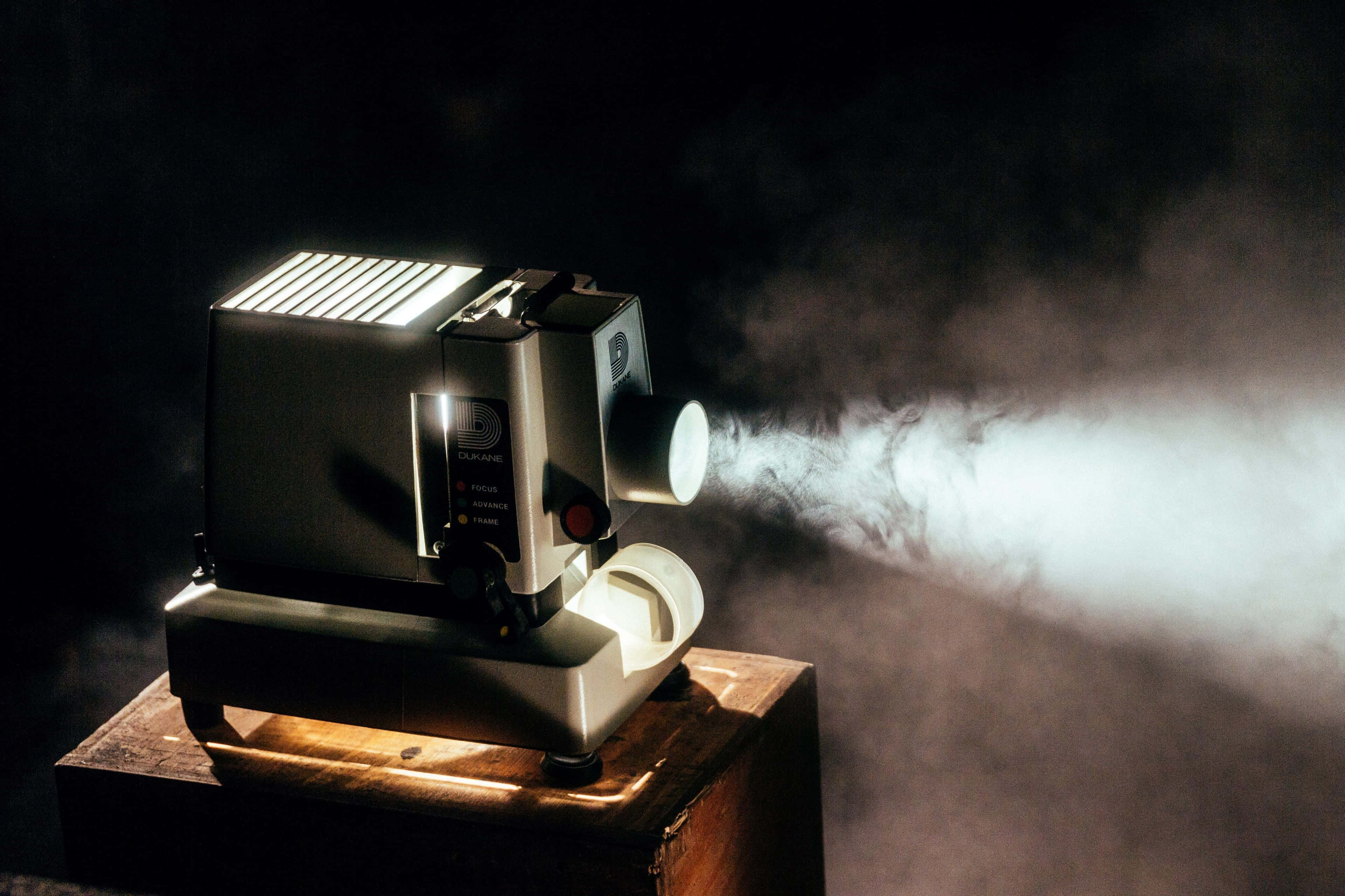4K Projector 桌布 壁紙 — 一部復古幻燈機在黑暗背景下，透過旋轉的煙霧投射出明亮的白光。