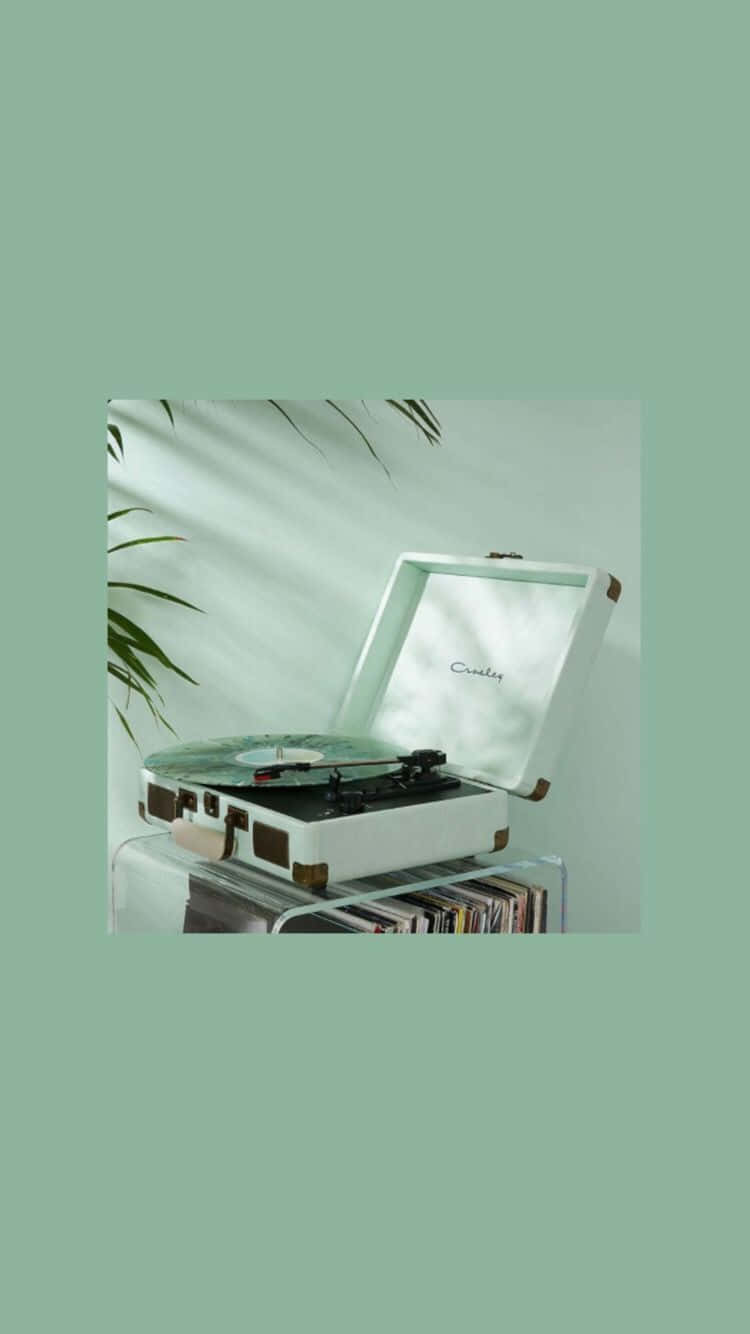 turntable 桌布 壁紙 — 一部復古白色行李箱式唱盤機放在玻璃架上，下方有黑膠唱片，以柔和的薄荷綠色牆壁為背景，襯托著綠色棕櫚葉。