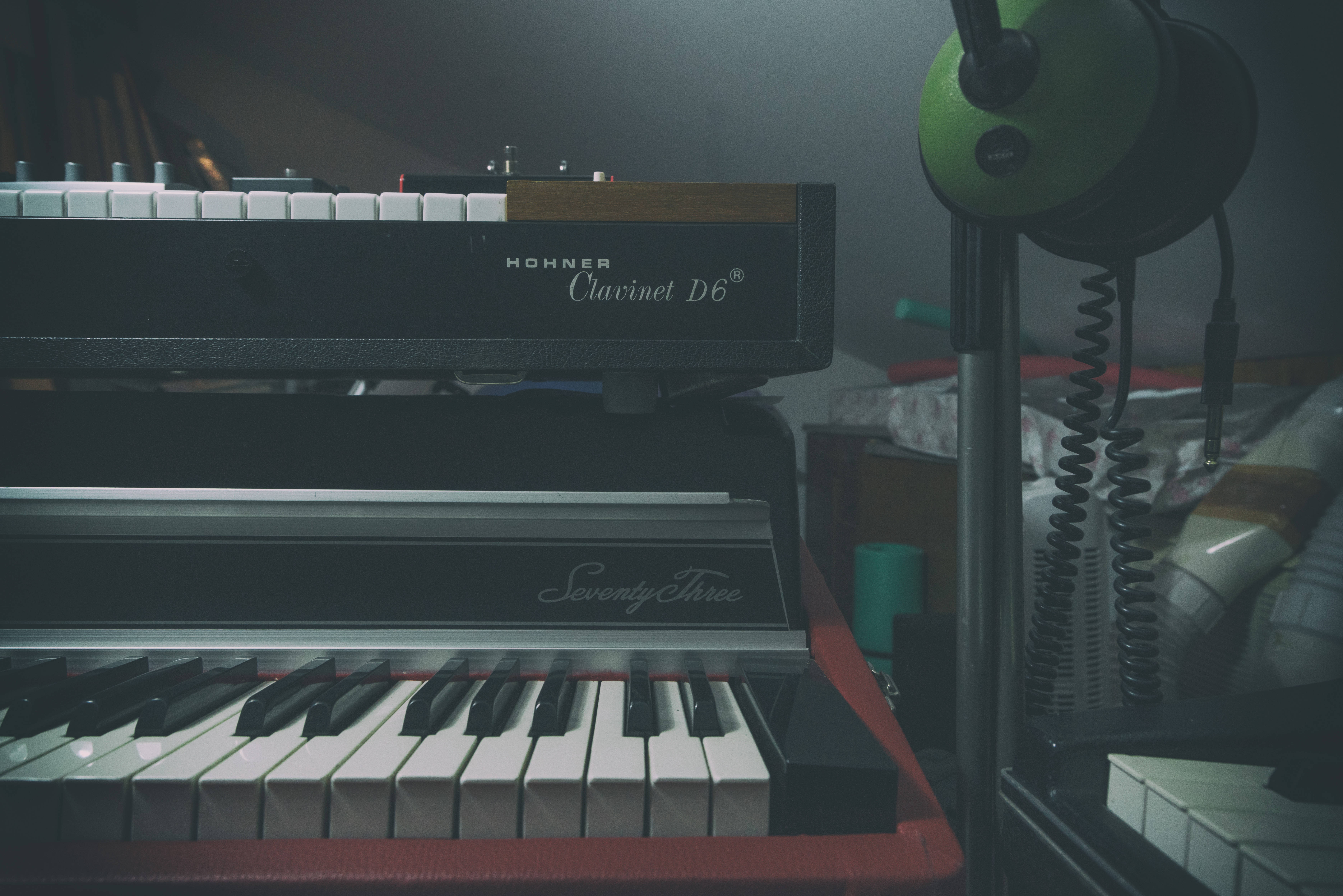 鋼琴 桌布 壁紙 — 一部復古的Hohner Clavinet D6和Seventy Three鍵盤放在昏暗的燈光下，附近有一個綠色的耳機架。