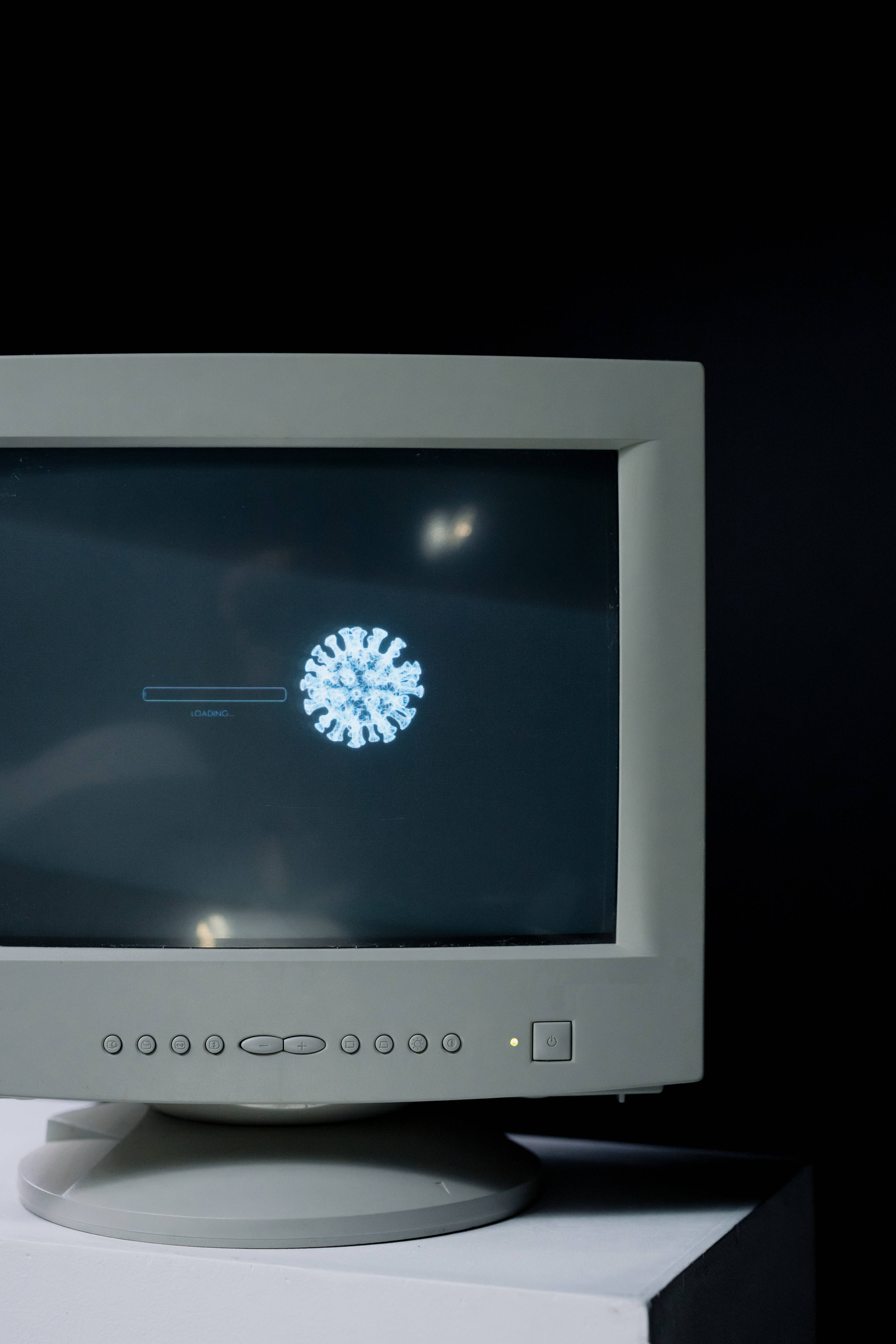 Computer Screen 桌布 壁紙 — 一部復古米色CRT顯示器在極簡工作室環境中，於黑暗螢幕上顯示發光的藍色病毒粒子圖形。