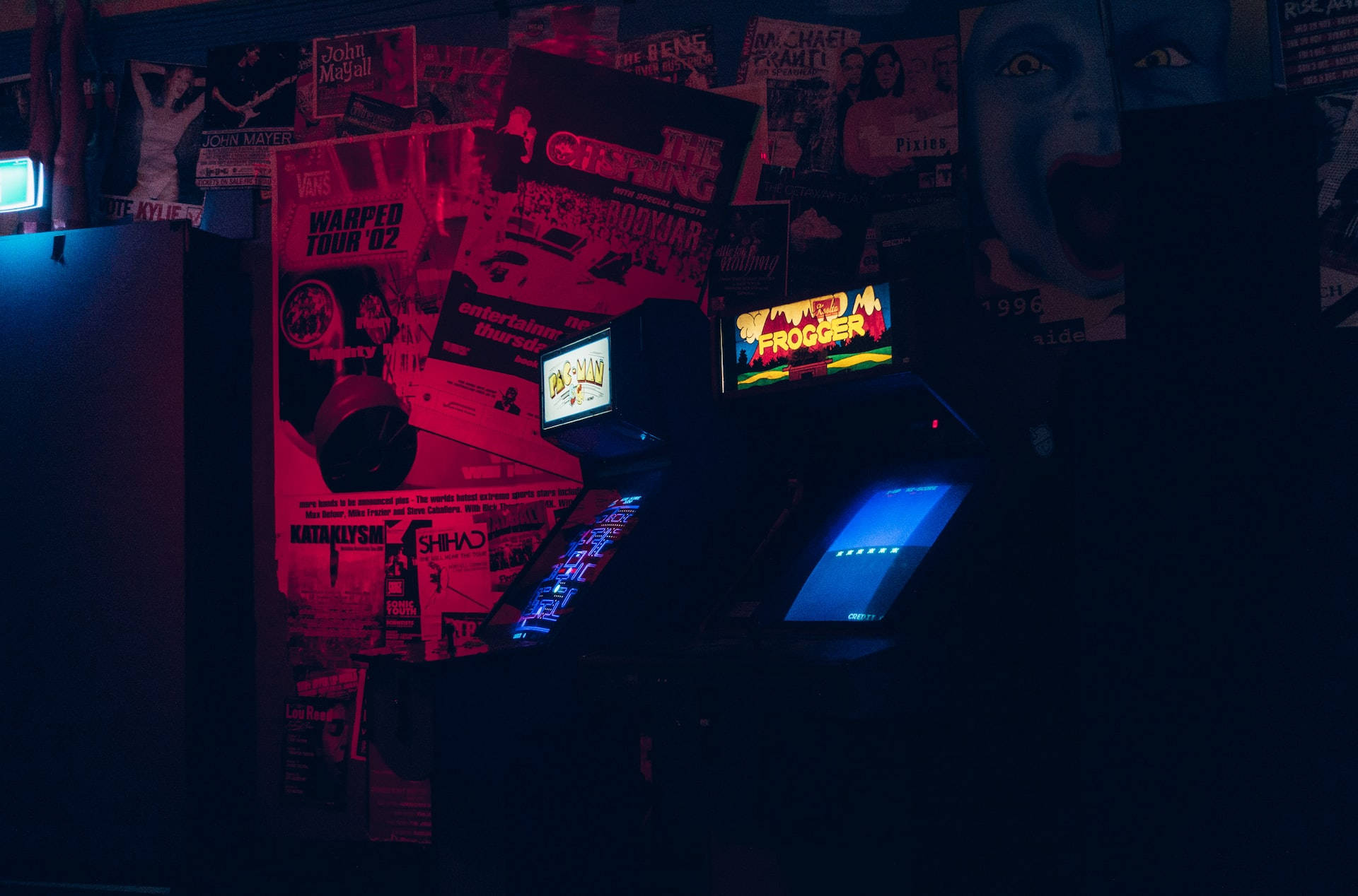 Night Aesthetic 桌布 壁紙 — 一部復古街機在昏暗的房間裡閃爍著霓虹燈光，房間裡貼滿了龐克搖滾海報。