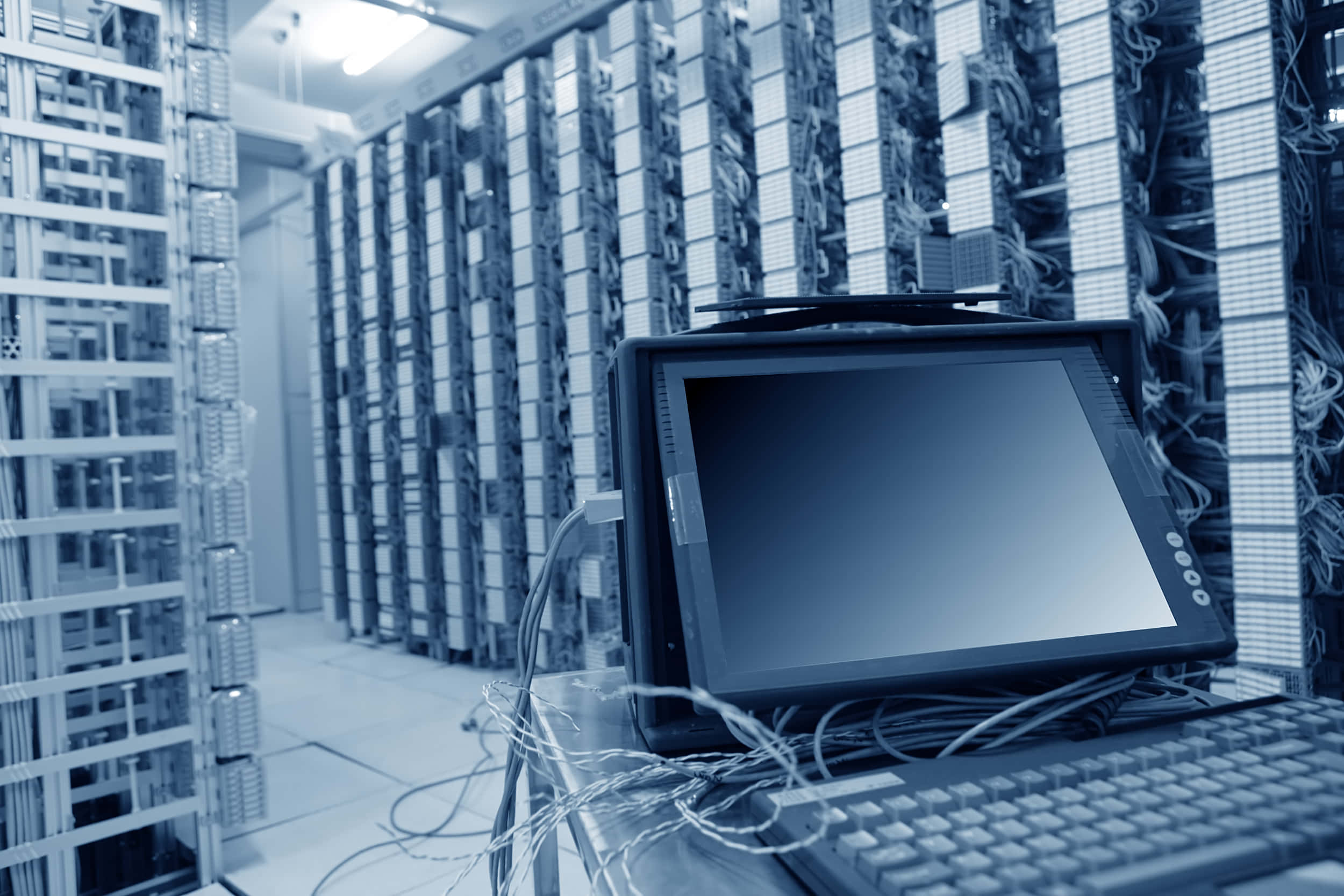 Data Management 桌布 壁紙 — 一部復古電腦終端機放置在冷色調藍色資料中心的高聳伺服器機架之間。