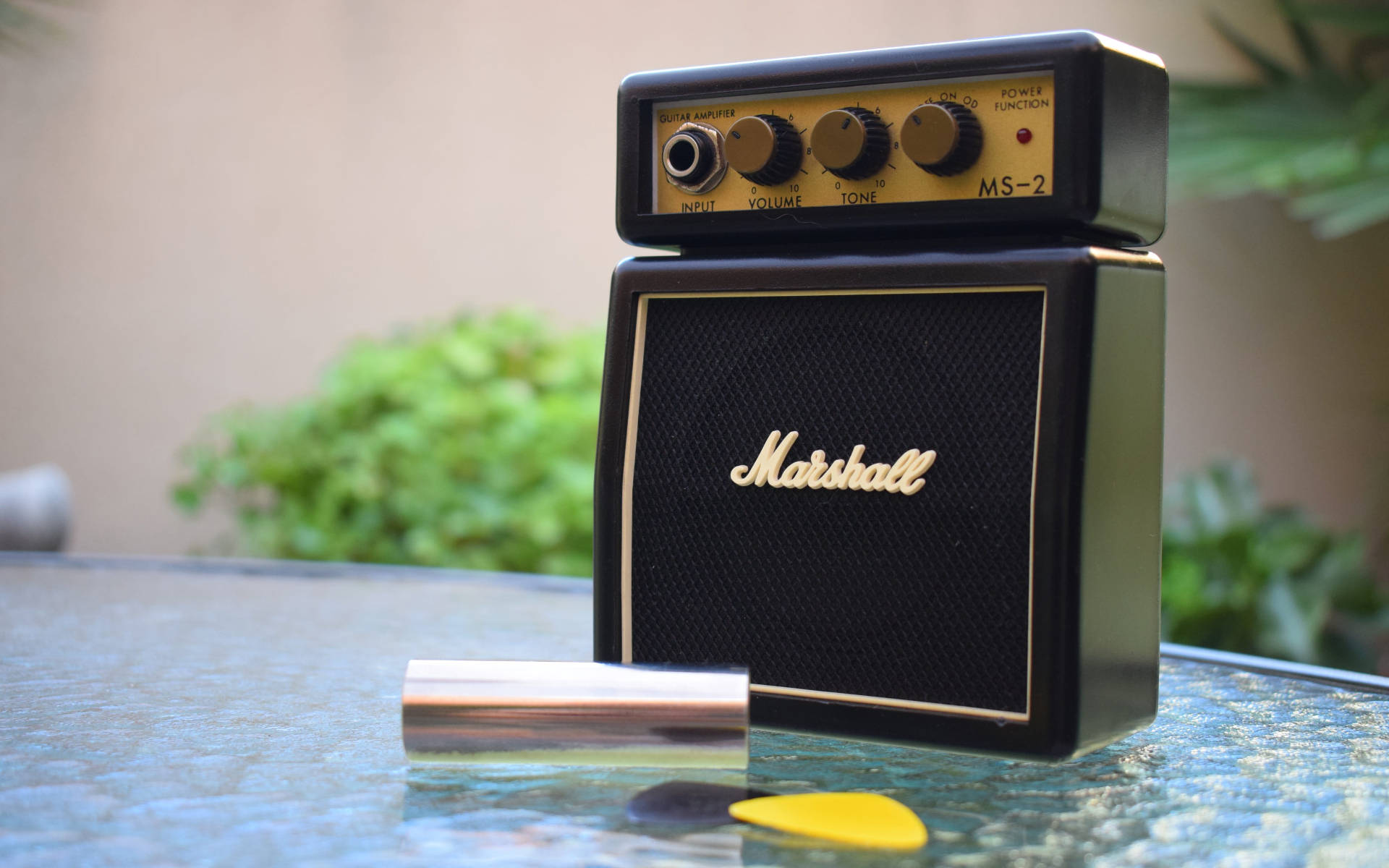 Marshall 桌布 壁紙 — 一部復古黑色Marshall MS-2吉他音箱放在玻璃桌上，旁邊有黃色撥片和銀色管子。
