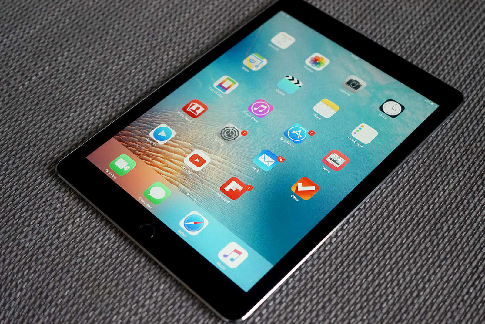 iPad 桌布 壁紙 — 一部時尚平板電腦，帶有鮮豔的應用程式網格，斜放在有紋理的灰色布料表面上。