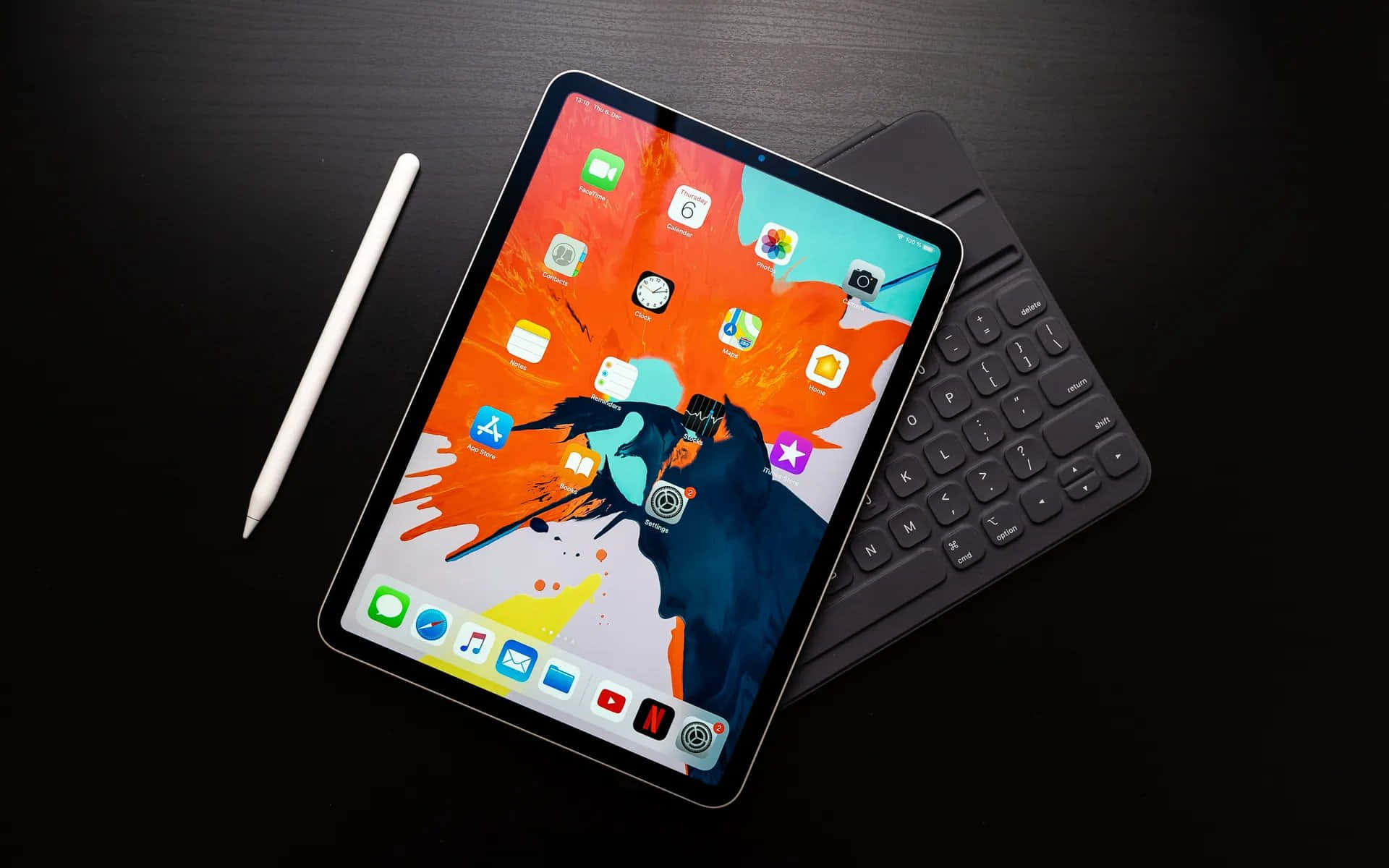 iPad 桌布 壁紙 — 一部時尚平板電腦帶有鮮豔的抽象桌布，放置在深色表面上，旁邊是其鍵盤保護套和白色觸控筆。