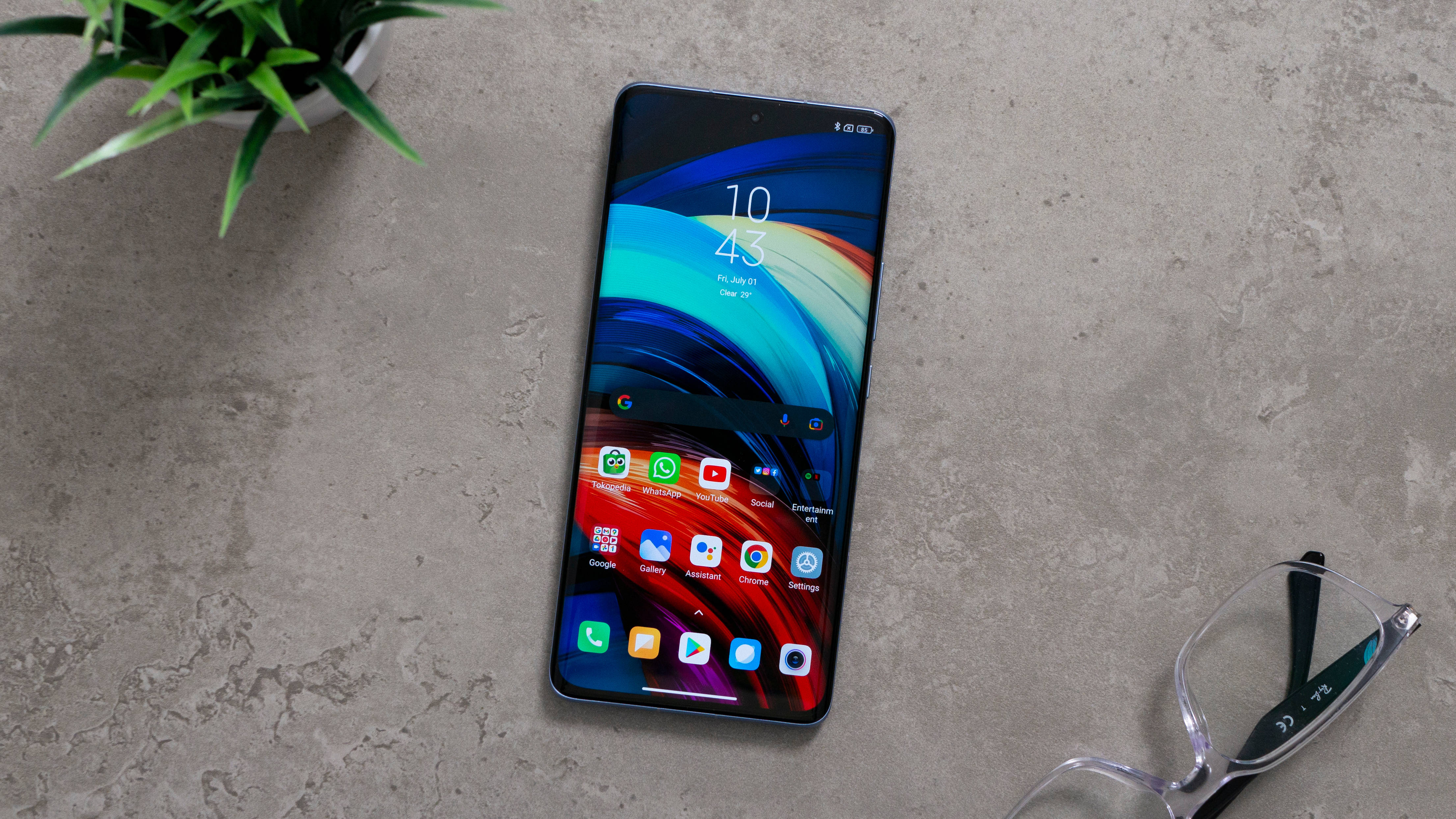 Xiaomi 桌布 壁紙 — 一部時尚智慧型手機帶有鮮豔的抽象桌布，放置在紋理混凝土表面上，旁邊有盆栽植物和閱讀眼鏡。