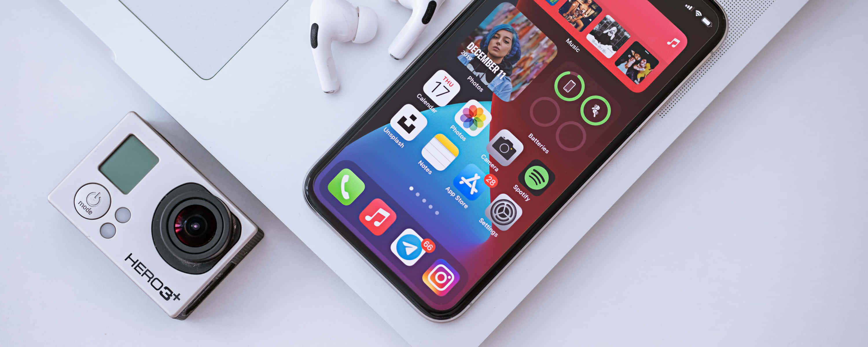 iPhone 桌布 壁紙 — 一部時尚智慧型手機顯示色彩繽紛的應用程式圖標，旁邊放著白色筆記型電腦和GoPro相機，置於簡約白色表面上。
