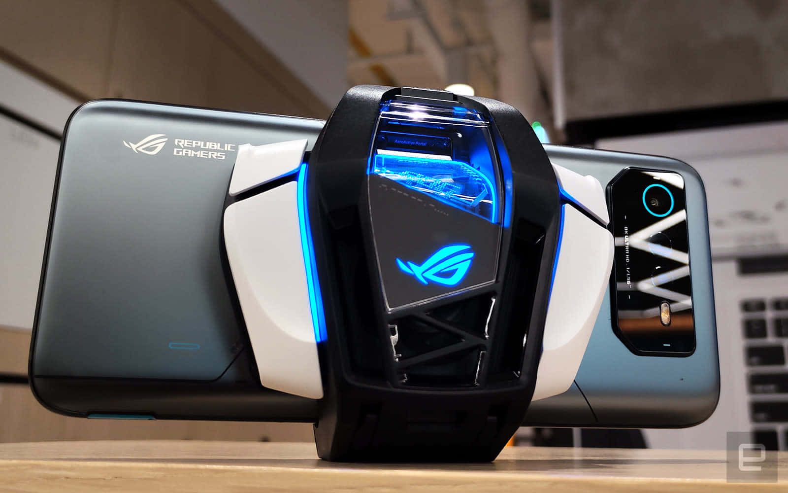 ASUS 桌布 壁紙 — 一部時尚的 ROG 遊戲智慧型手機，背面裝有發光藍色冷卻配件，展示在木質表面上。