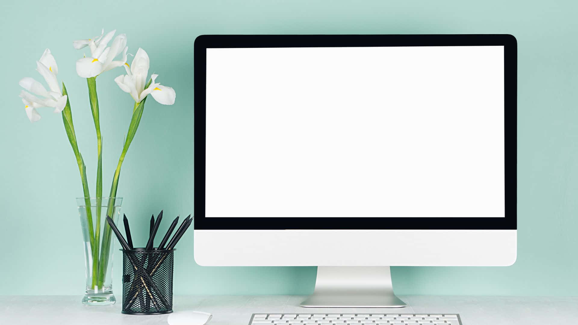 Computer Screen 桌布 壁紙 — 一部時尚的iMac放在乾淨的桌子上，旁邊放著一瓶白色鳶尾花和一個筆筒，背景是柔和的青綠色牆壁。