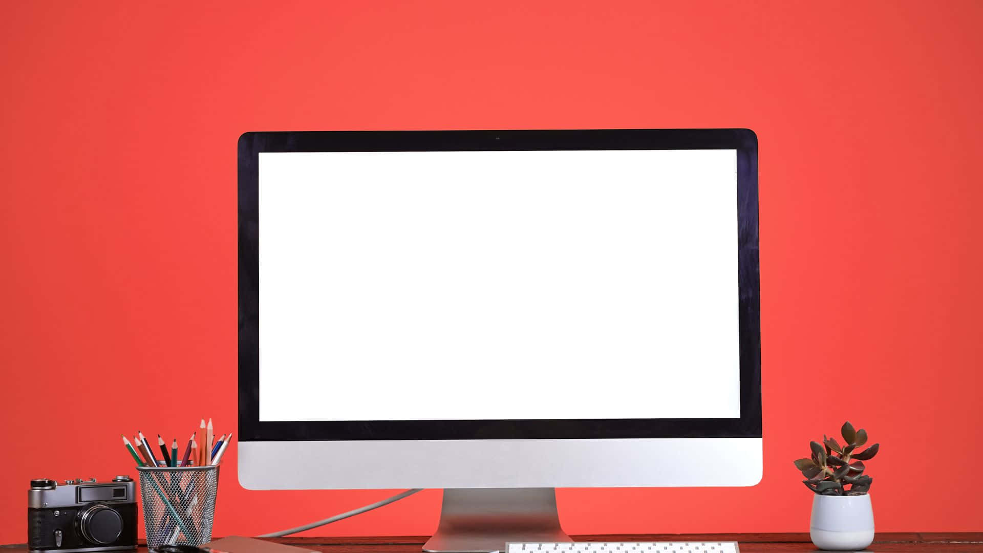 Computer Screen 桌布 壁紙 — 一部時尚的iMac放在木桌上，背景是鮮紅色的牆壁，旁邊有一個相機筆筒和盆栽多肉植物。