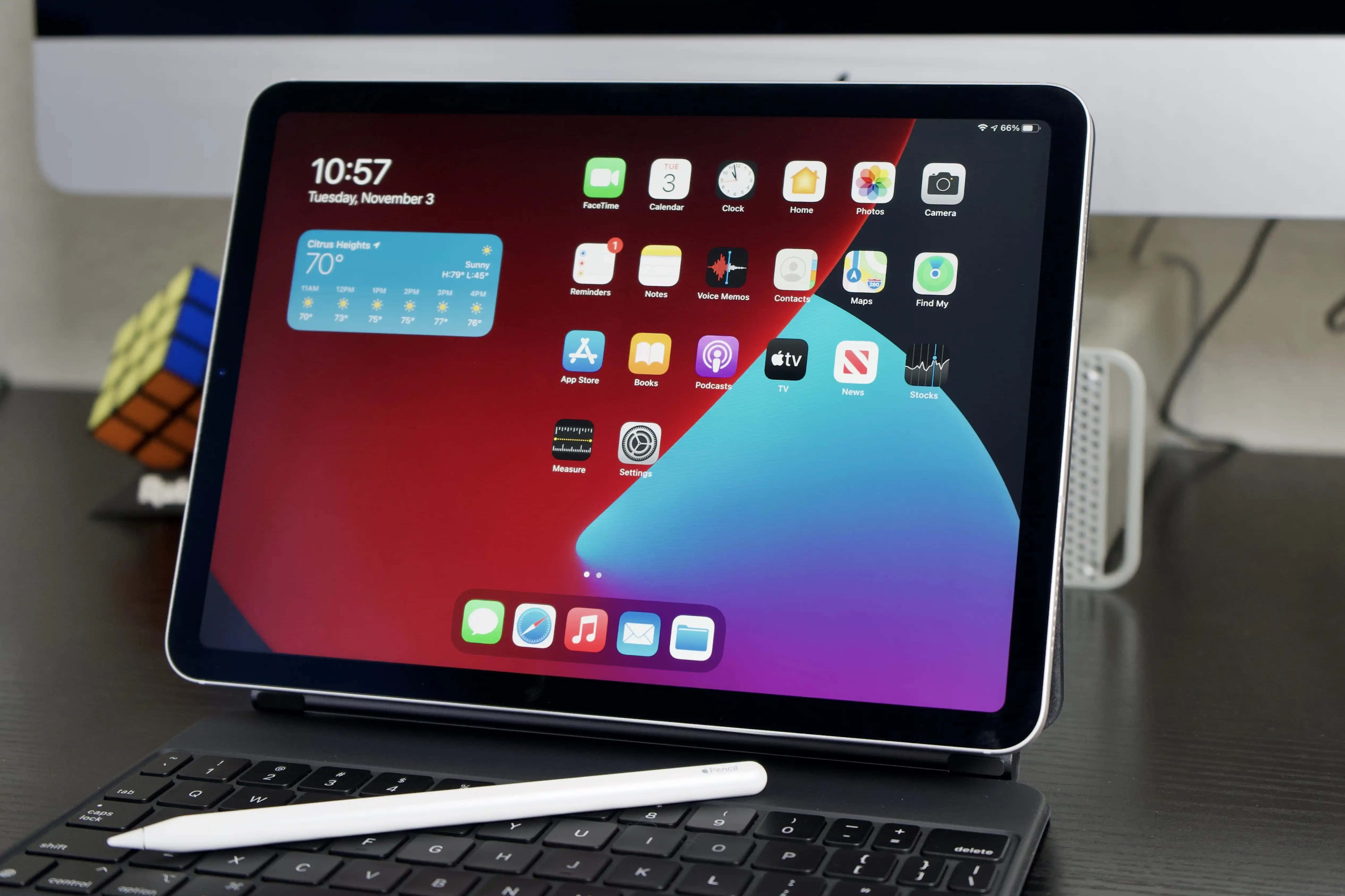 iPad 桌布 壁紙 — 一部時尚的iPad Pro帶有鮮豔漸層桌布，放在鍵盤上，觸控筆在附近，旁邊是暗色桌上的魔術方塊。