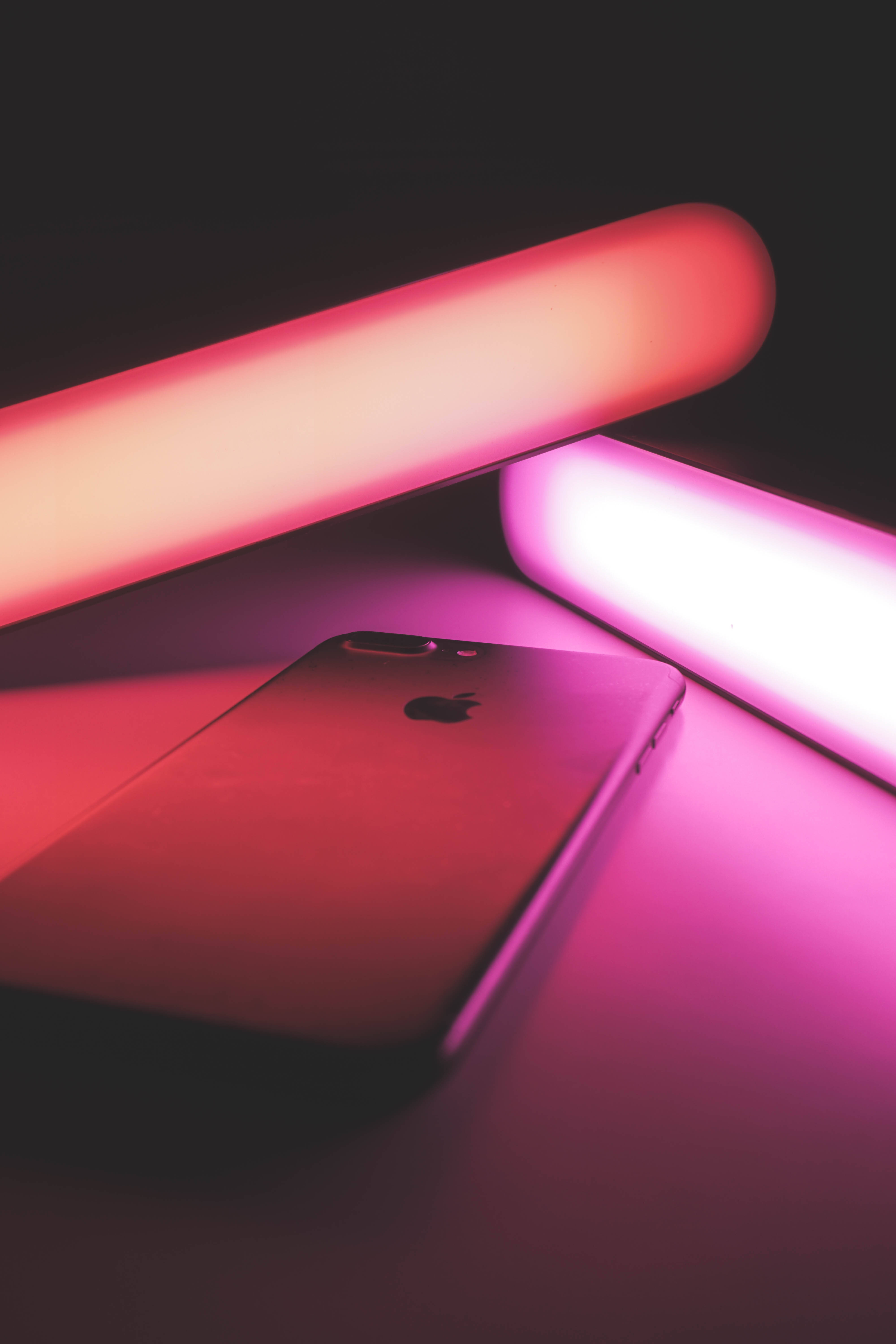 紫色 iPhone 桌布 壁紙 — 一部時尚的iPhone在發光的粉紅色和紅色霓虹燈管下，在黑暗的表面上投射出鮮豔的光芒。
