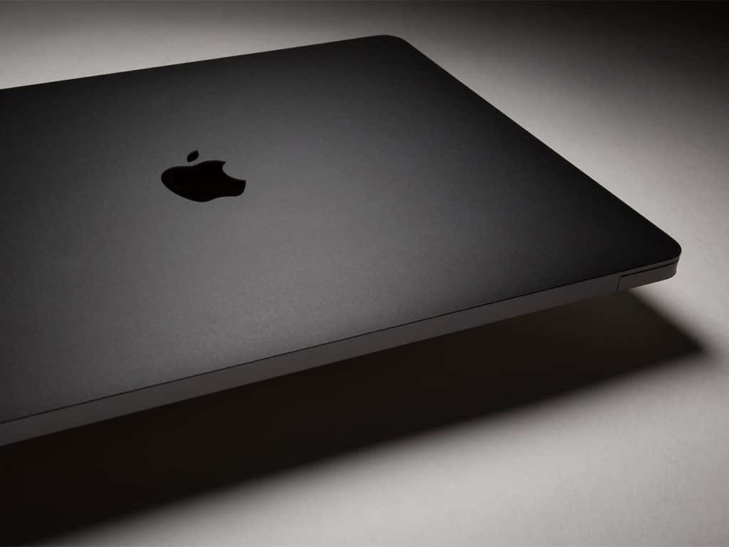 Black Macbook 桌布 壁紙 — 一部時尚的啞光黑色筆記型電腦，帶有簡約的Apple標誌，在柔和的工作室燈光下傾斜放置。