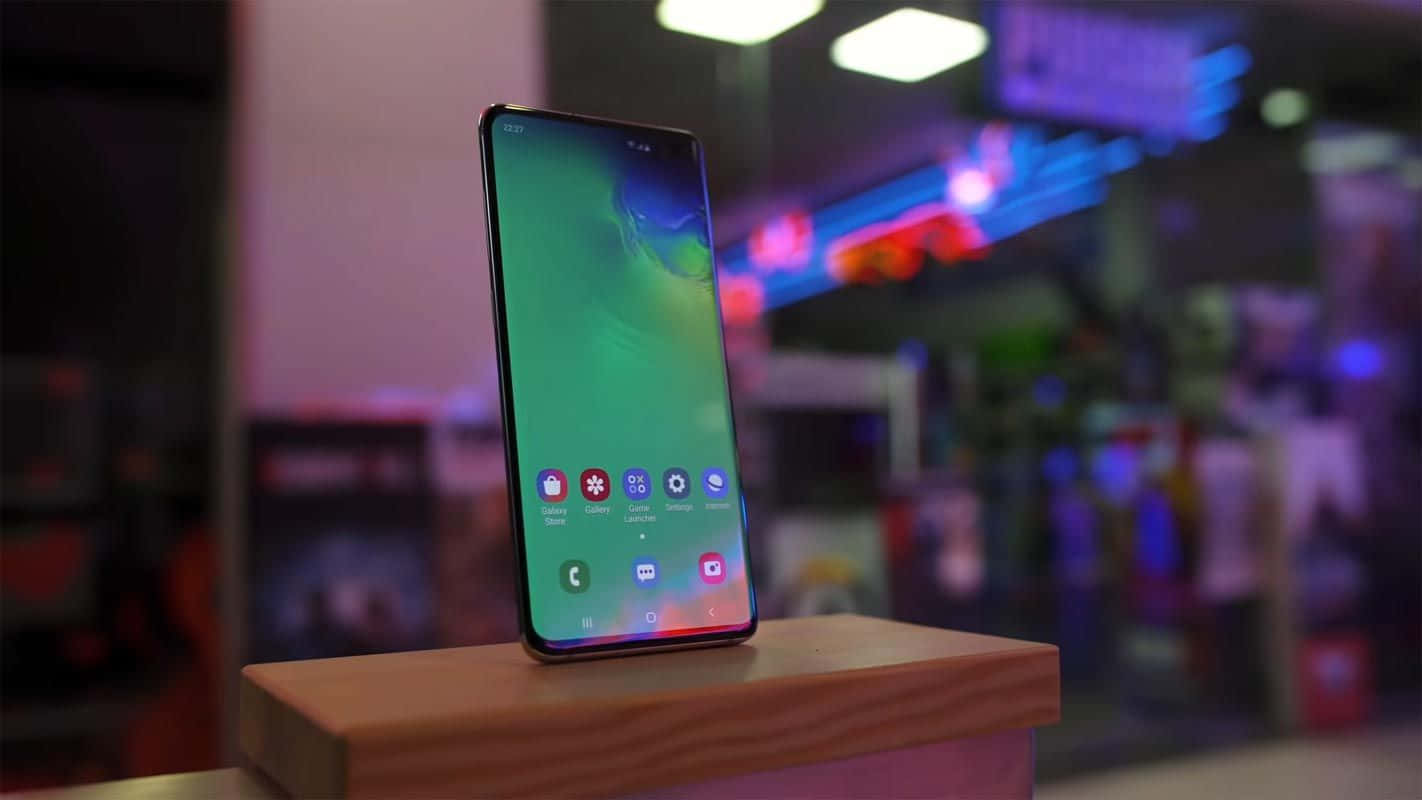 Galaxy S10 桌布 壁紙 — 一部時尚的智慧型手機，帶有充滿活力的綠色螢幕，直立於木塊上，背景是模糊的霓虹燈城市景觀。