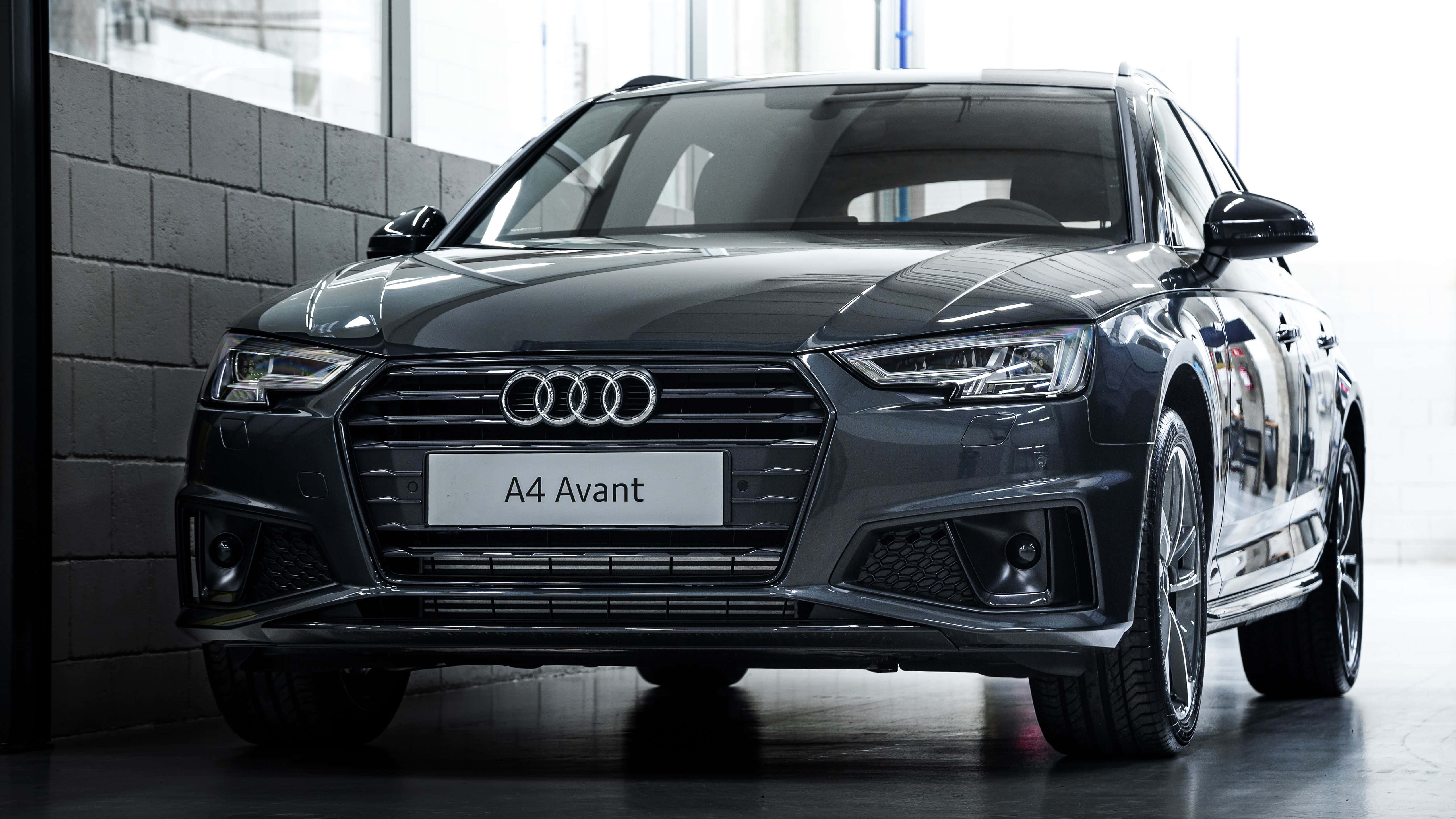 Audi A4 桌布 壁紙 — 一部時尚的深灰色奧迪 A4 Avant 旅行車在現代室內工作室中展示，配有反射地板和灰色磚牆背景。