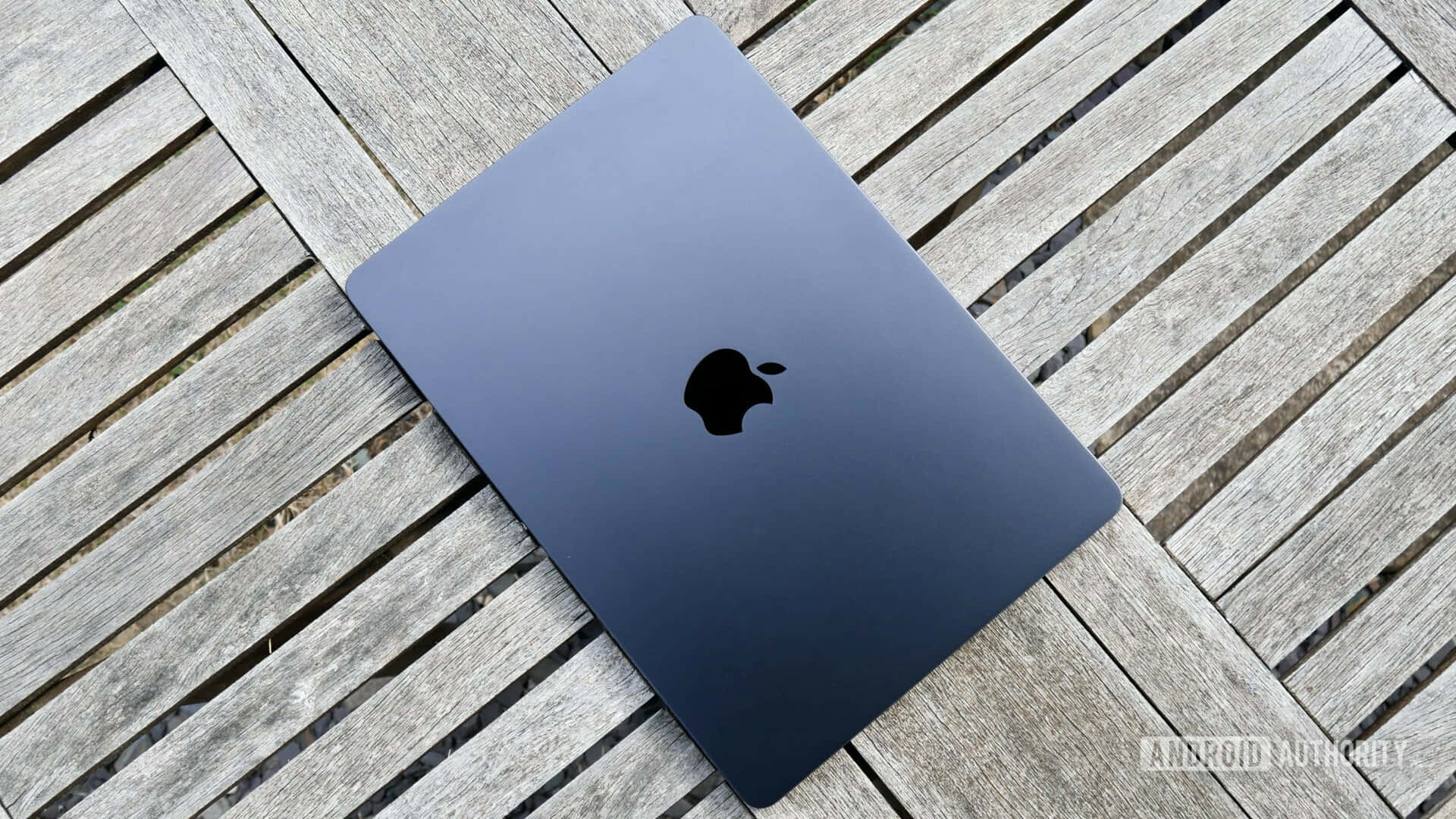 MacBook 動態圖片 桌布 壁紙 — 一部時尚的深藍色 MacBook 闔上放在經風化的灰色木板上，在自然日光下。
