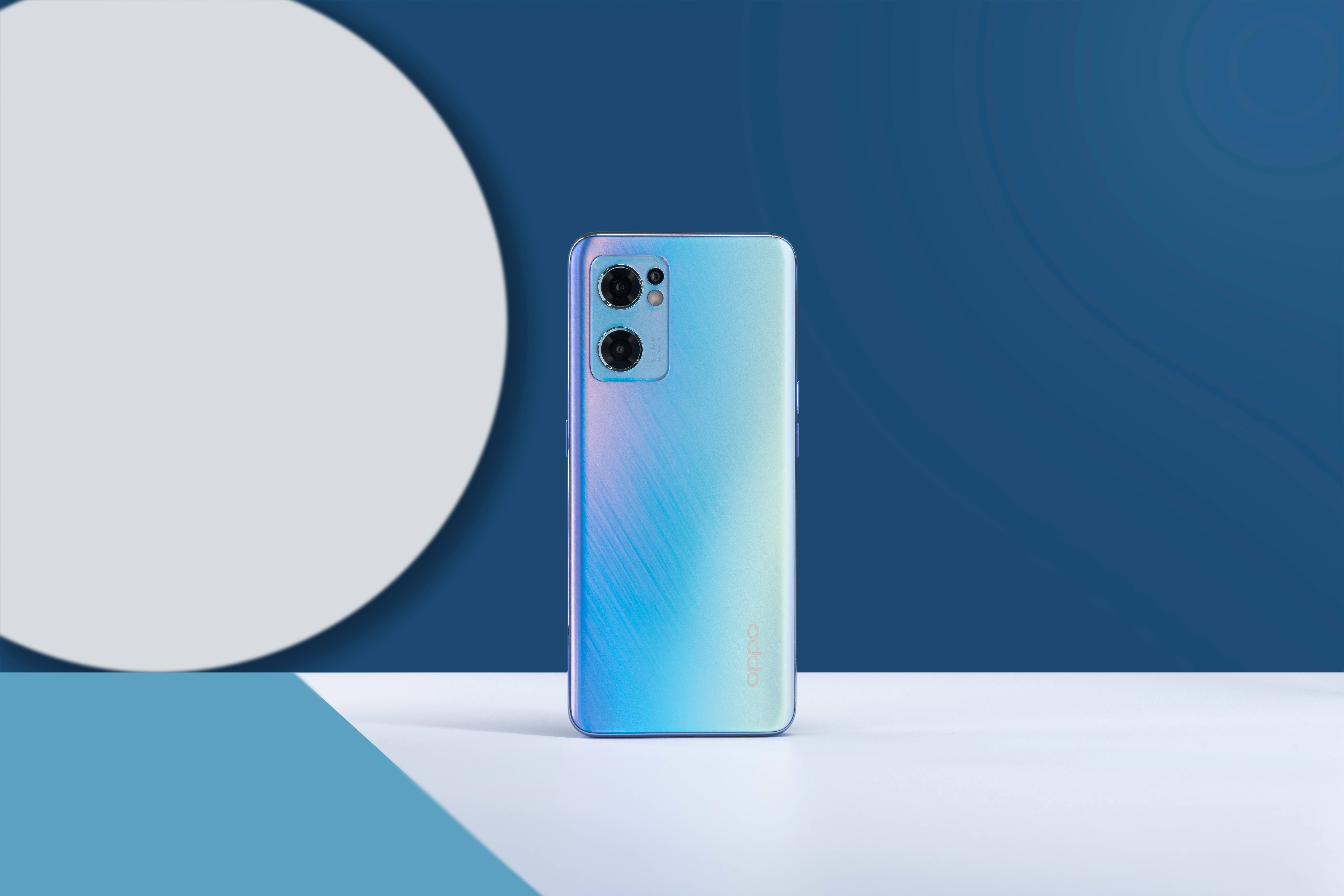 oppo 桌布 壁紙 — 一部時尚的漸變藍色智慧型手機，配備雙鏡頭，直立於白色表面上，背景為現代藍白圓形圖案。