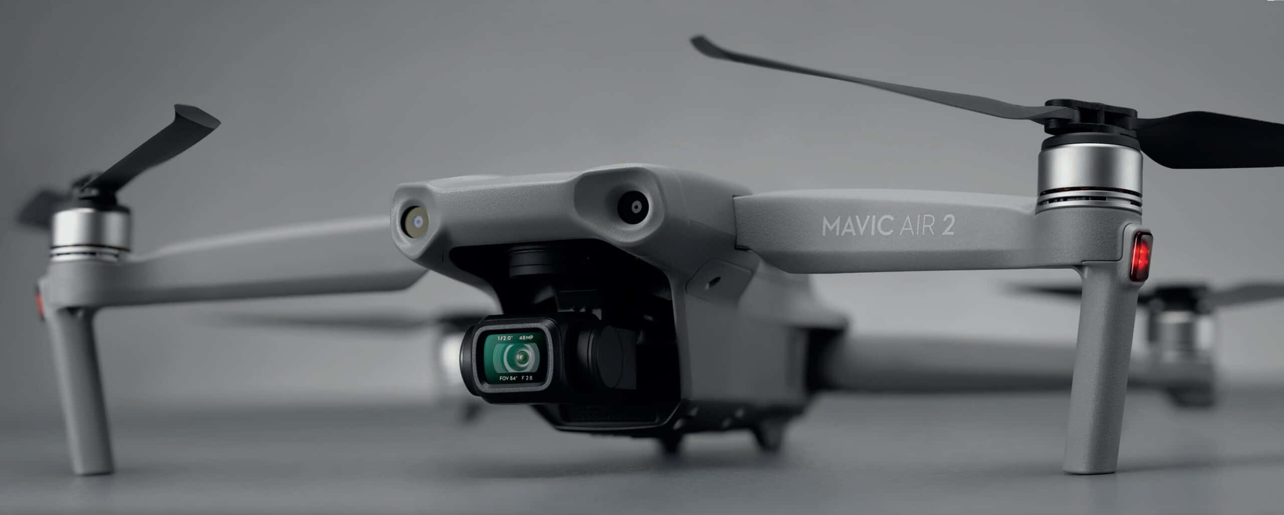 Imminent 桌布 壁紙 — 一部時尚的灰色DJI Mavic Air 2無人機，配備黑色螺旋槳和綠色鏡頭，放置在柔和的灰色工作室背景前。