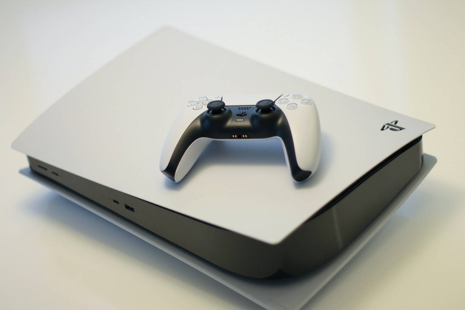 Xbox One X 桌布 壁紙 — 一部時尚的白色 PlayStation 5 主機和一個相配的控制器，在柔和燈光下放置在簡約的白色表面上。
