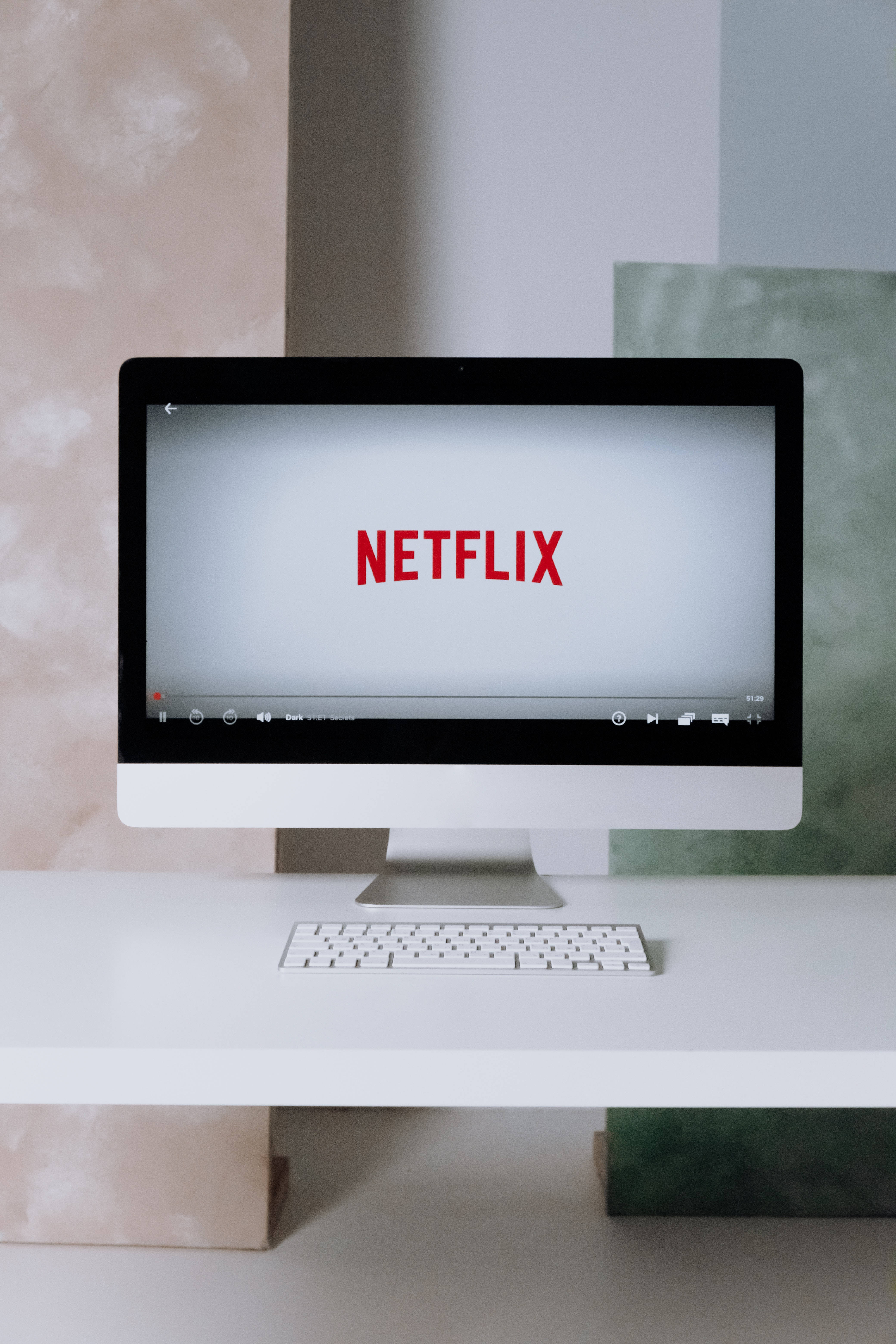 Computer Screen 桌布 壁紙 — 一部時尚的白色iMac在簡約的桌子上顯示紅色Netflix標誌，背景是柔和色調的軟質紋理牆壁。