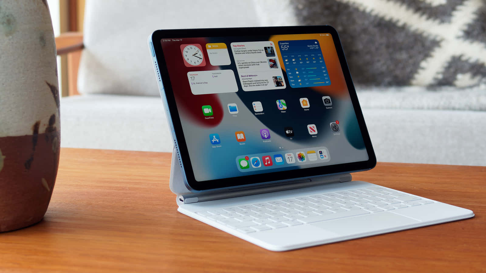 iPad 桌布 壁紙 — 一部時尚的白色iPad連鍵盤保護套放在木桌上，旁邊有一個陶瓷花瓶，背景是舒適的客廳。