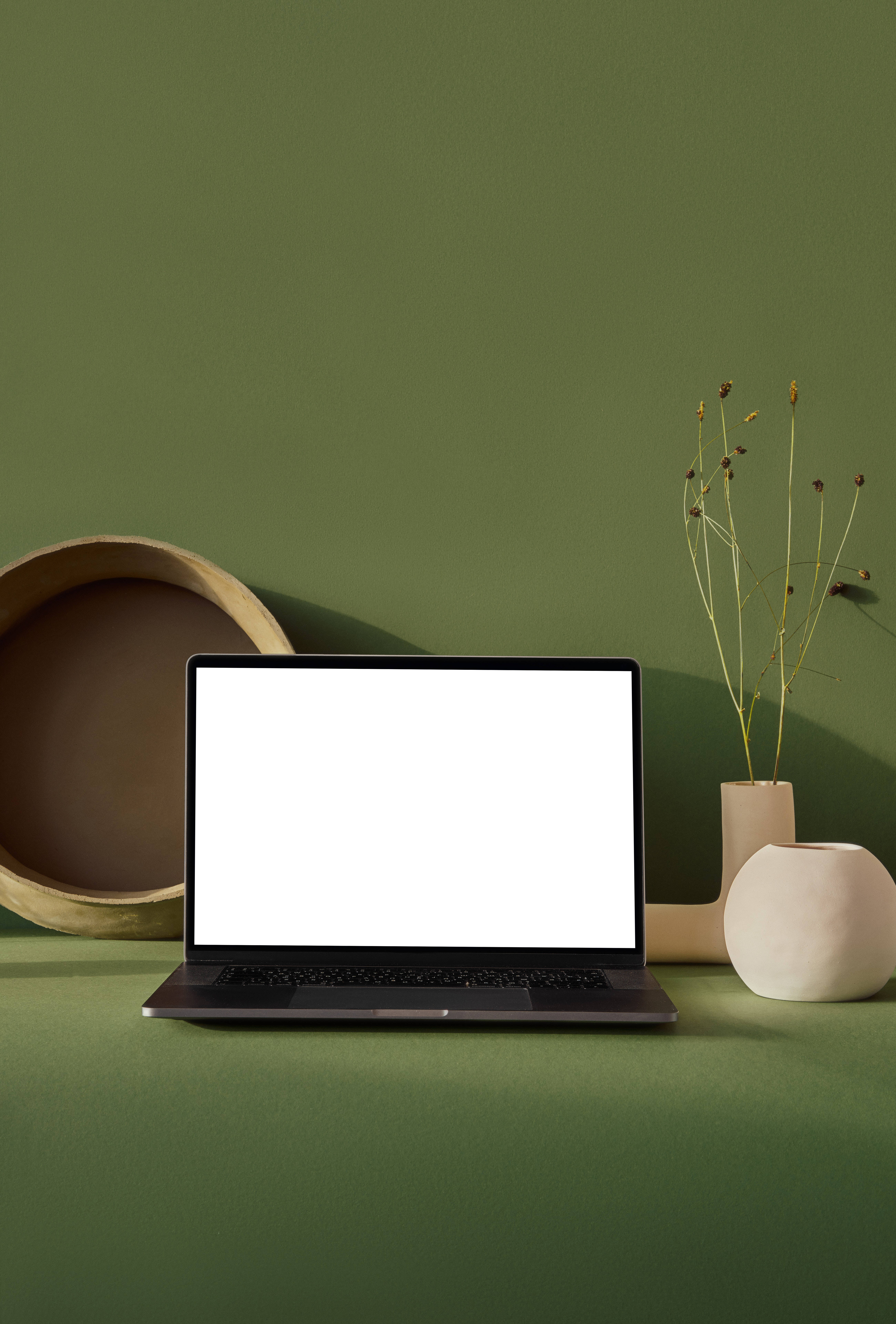 aesthetic tumblr laptop 桌布 壁紙 — 一部時尚的筆記型電腦，螢幕空白，放在綠色表面上，旁邊有簡約陶瓷裝飾和乾燥植物。