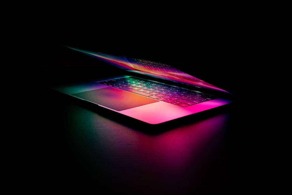 Best Laptop 桌布 壁紙 — 一部時尚的筆記型電腦在漆黑背景上散發出鮮豔的彩虹光芒。