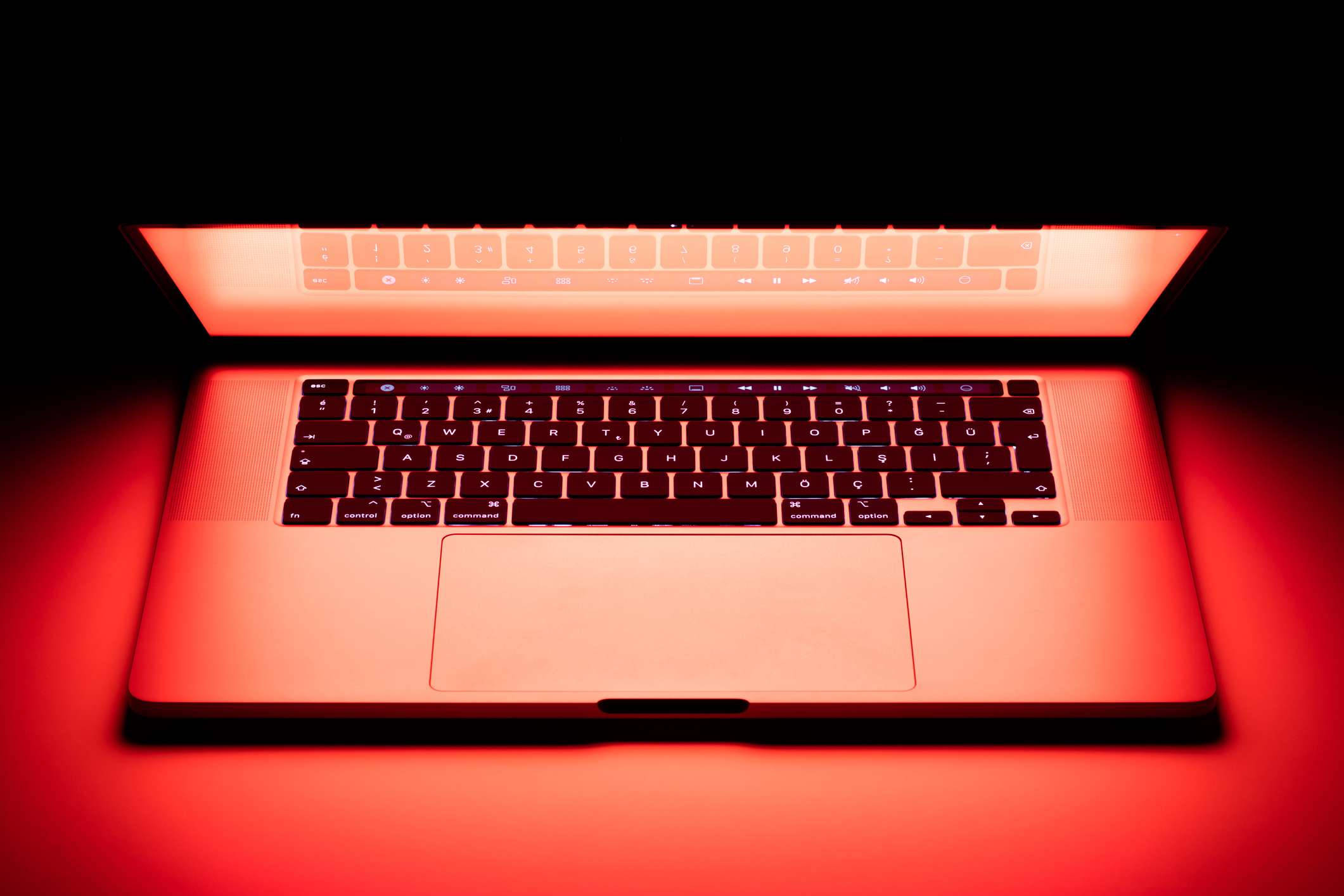 MacBook 動態圖片 桌布 壁紙 — 一部時尚的筆記型電腦在漆黑背景下發出強烈的紅光，在其銀色機身上投射出溫暖的環境光暈。