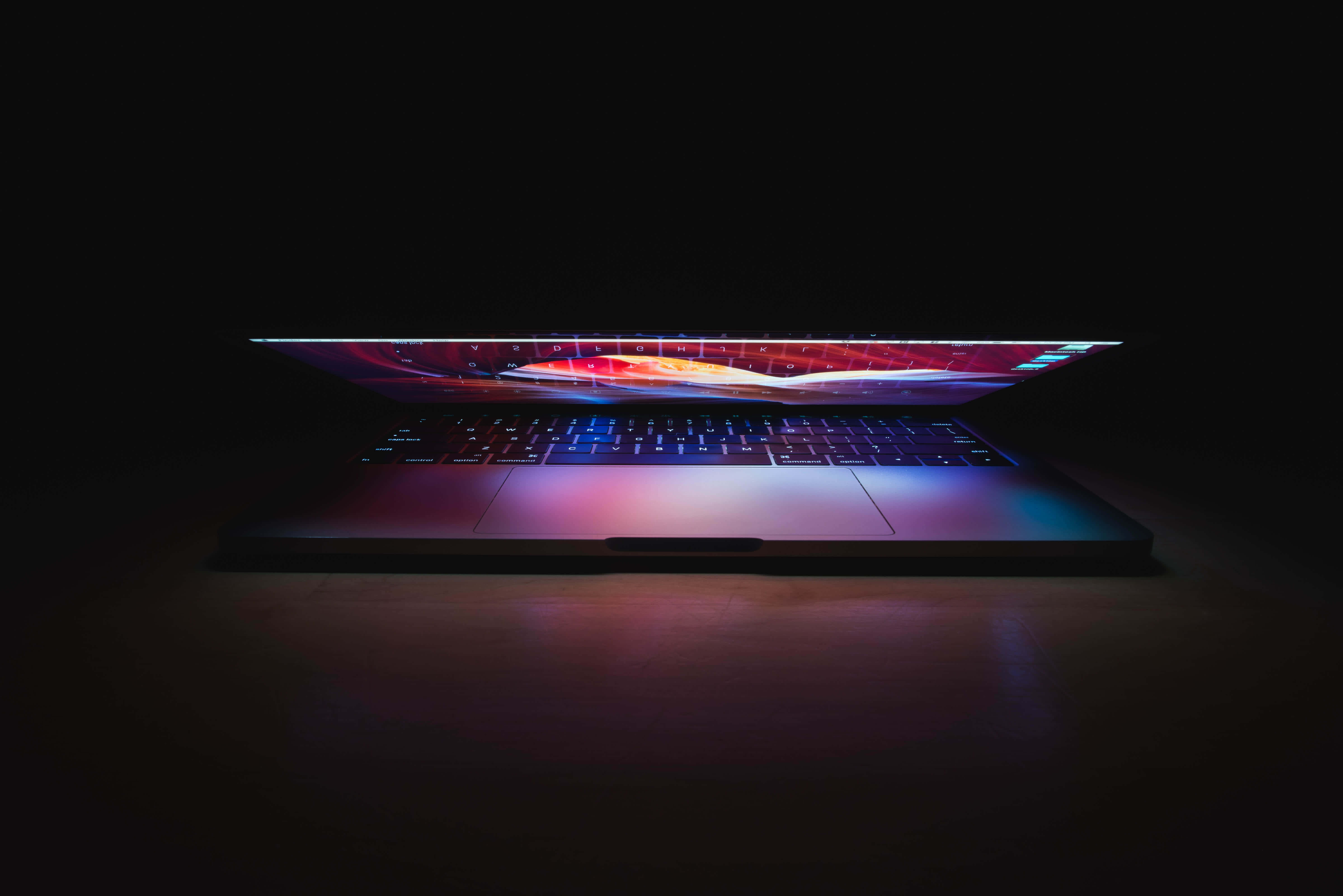 美學 MacBook 壁紙 桌布 壁紙 — 一部時尚的筆記型電腦在黑暗背景上，螢幕和鍵盤散發出充滿活力的抽象光芒。