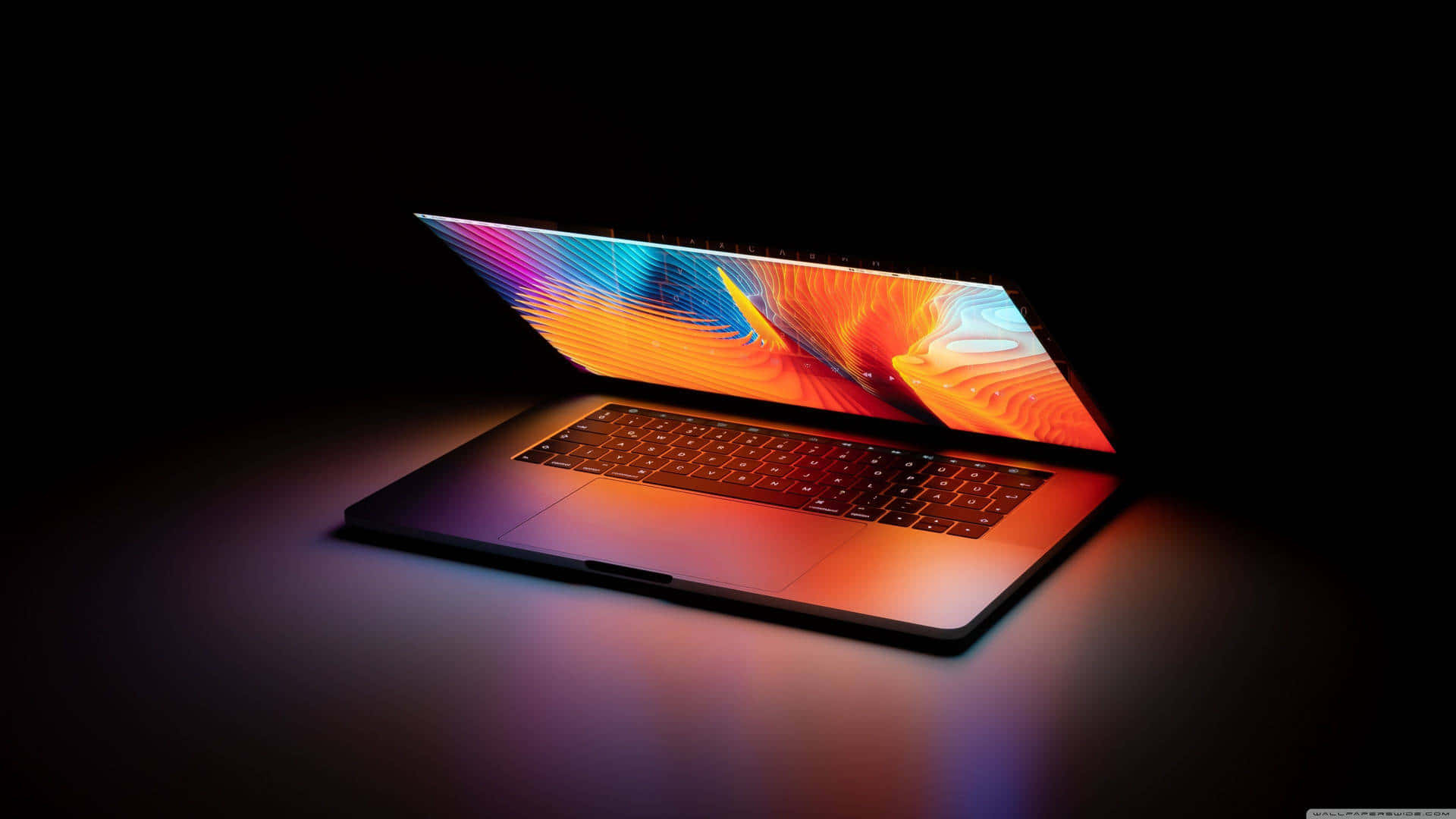 Black Macbook 桌布 壁紙 — 一部時尚的筆記型電腦在黑暗背景下，螢幕散發出鮮豔的抽象色彩。