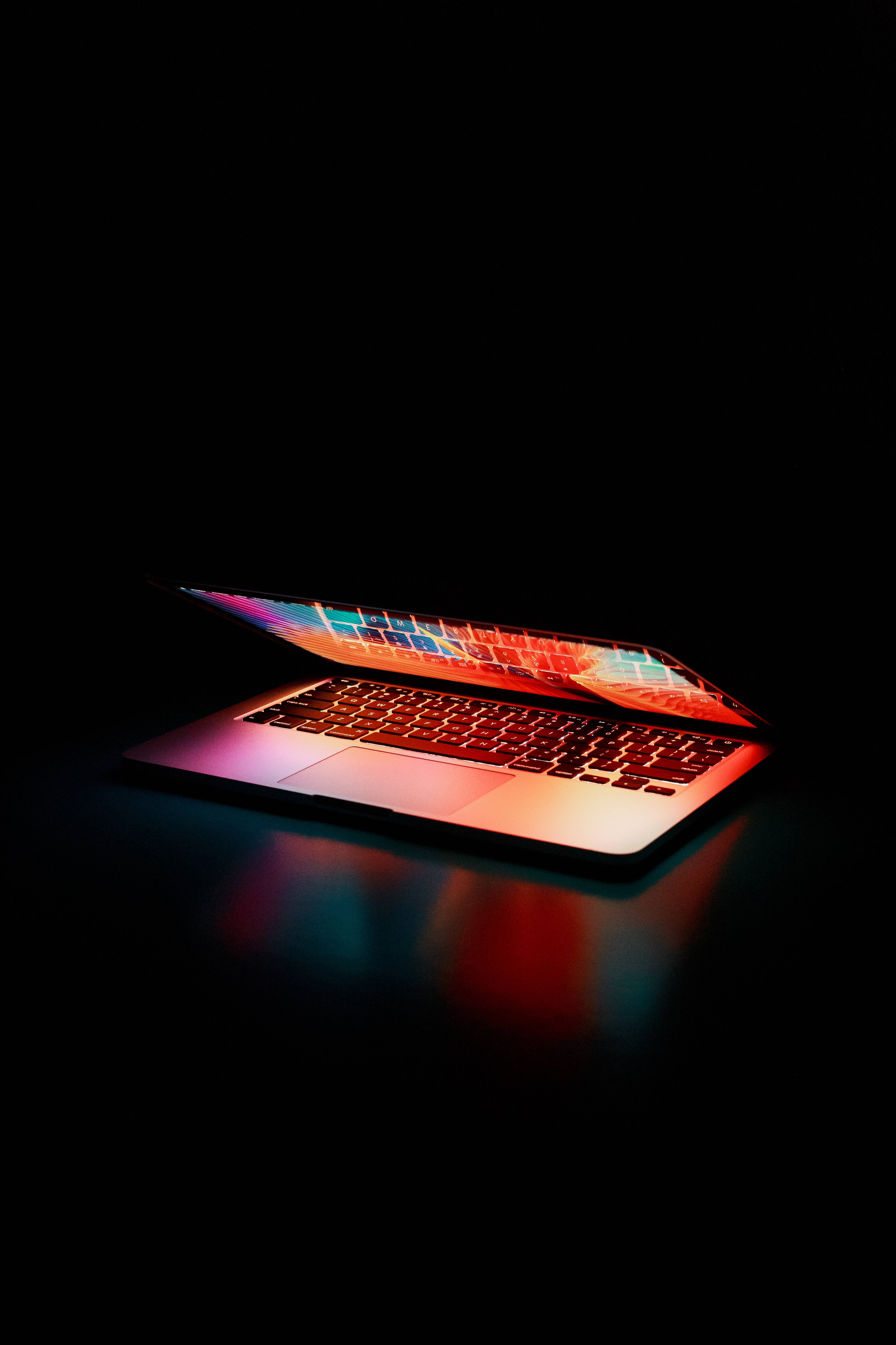 aesthetic tumblr laptop 桌布 壁紙 — 一部時尚的筆記型電腦在黑色背景的暗色表面上散發出鮮豔的霓虹反射光芒。