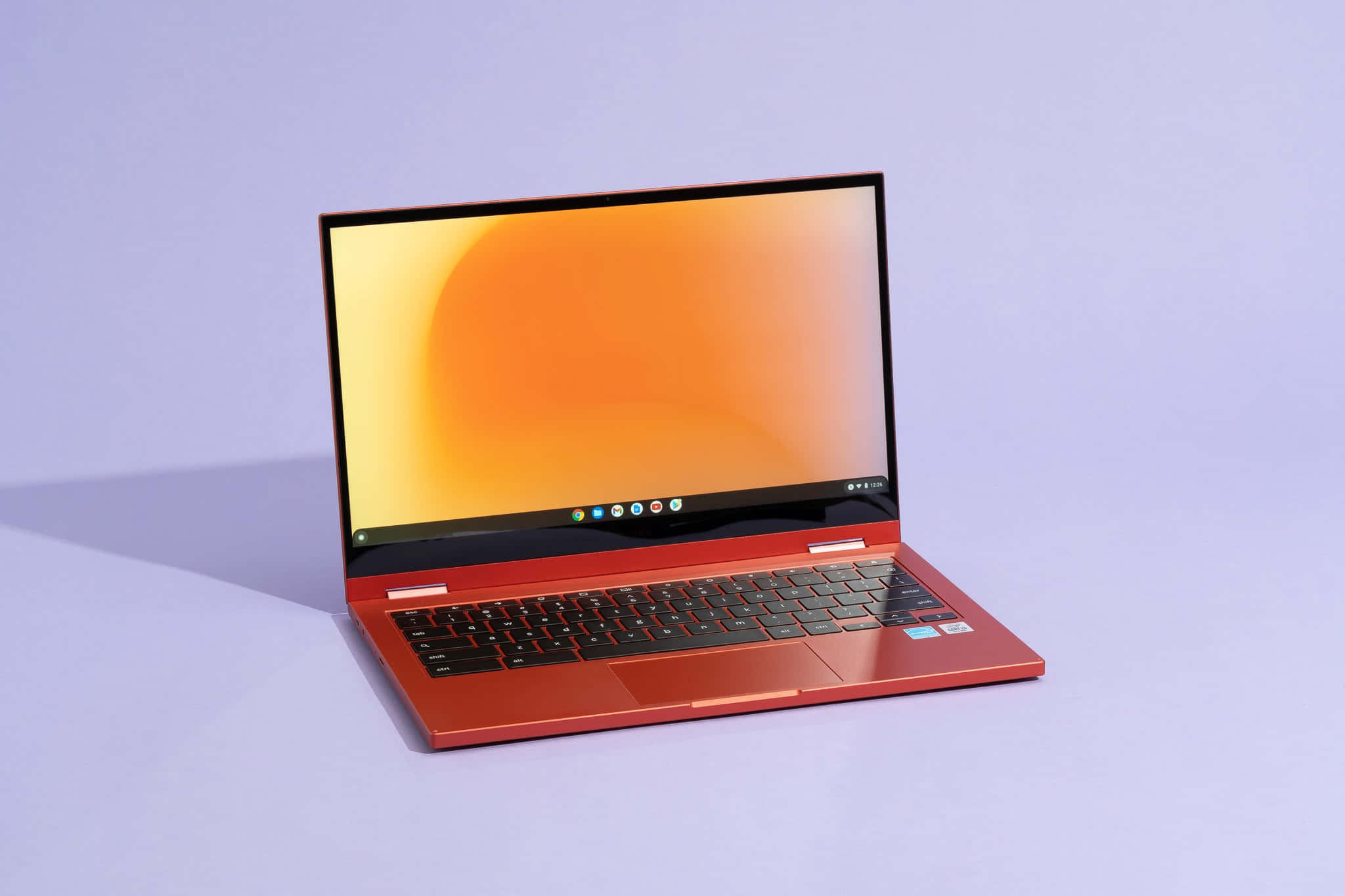 Chromebook 桌布 壁紙 — 一部時尚的紅色筆記型電腦，帶有發光的橙色螢幕，在明亮的攝影棚燈光下打開，放在柔軟的薰衣草表面上。