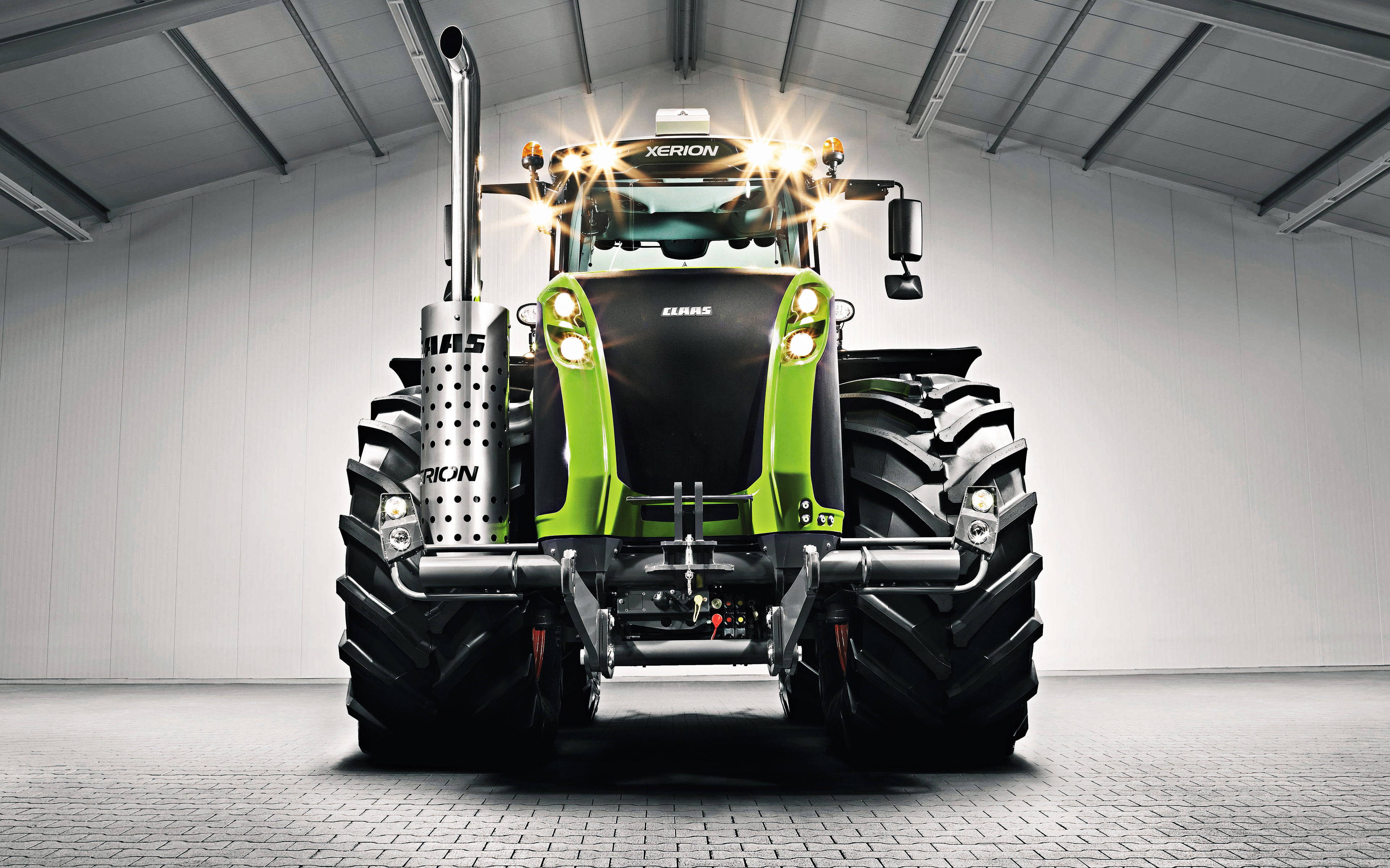 Farmhouse 桌布 壁紙 — 一部時尚的綠色和黑色Claas Xerion拖拉機，帶有發光的前燈，醒目地矗立在潔白的工業機庫中。