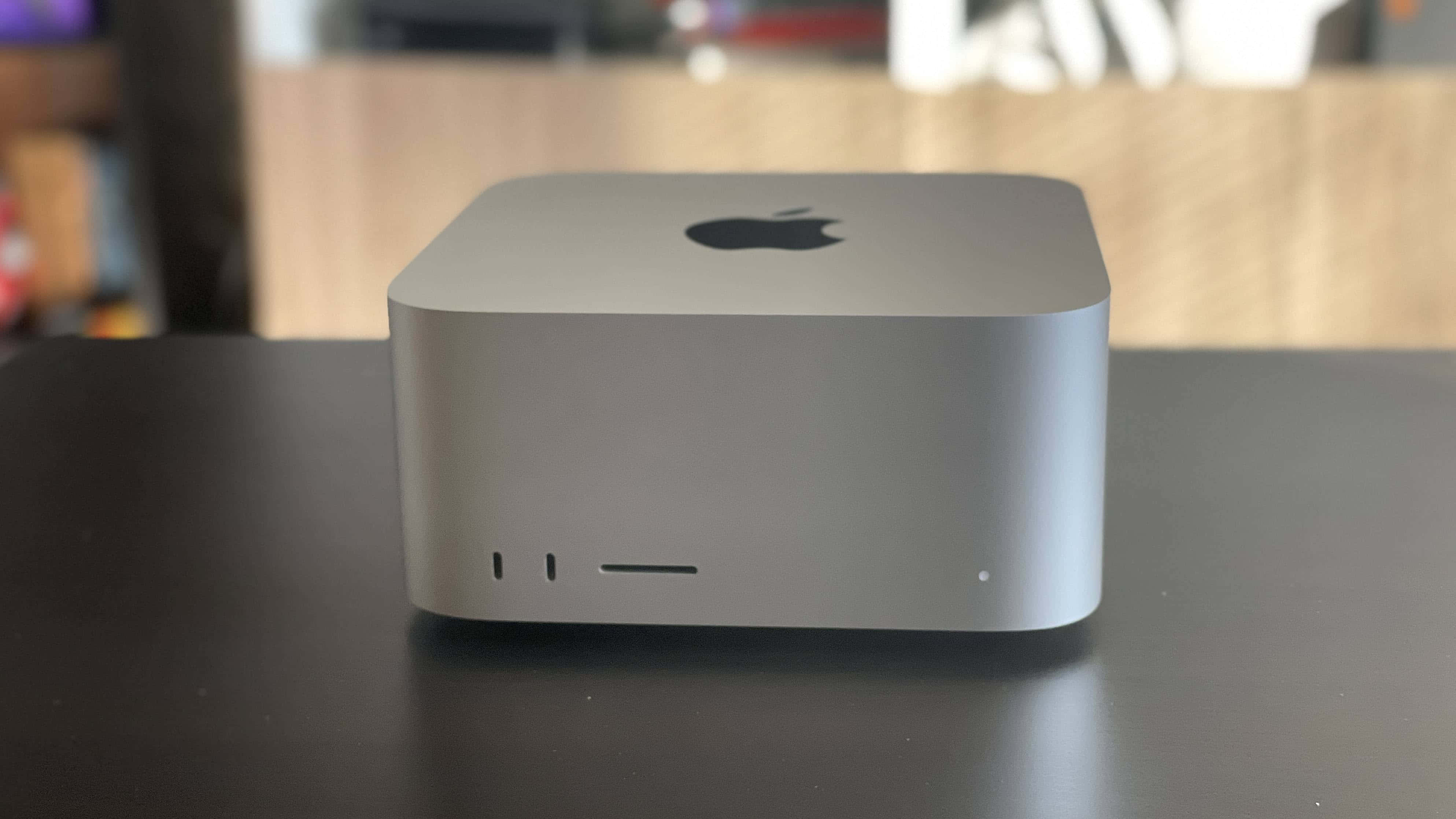 Mac 桌布 壁紙 — 一部時尚的銀色 Apple Mac mini 放置在深色桌子上，背景為模糊的木質。