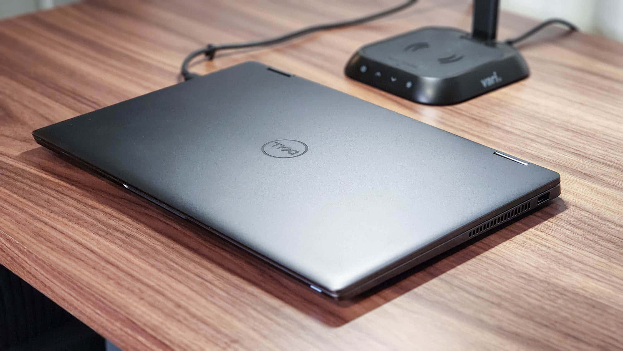 Dell 桌布 壁紙 — 一部時尚的銀色 Dell 筆記型電腦闔上放在溫暖的木桌上，旁邊有一個黑色無線路由器。