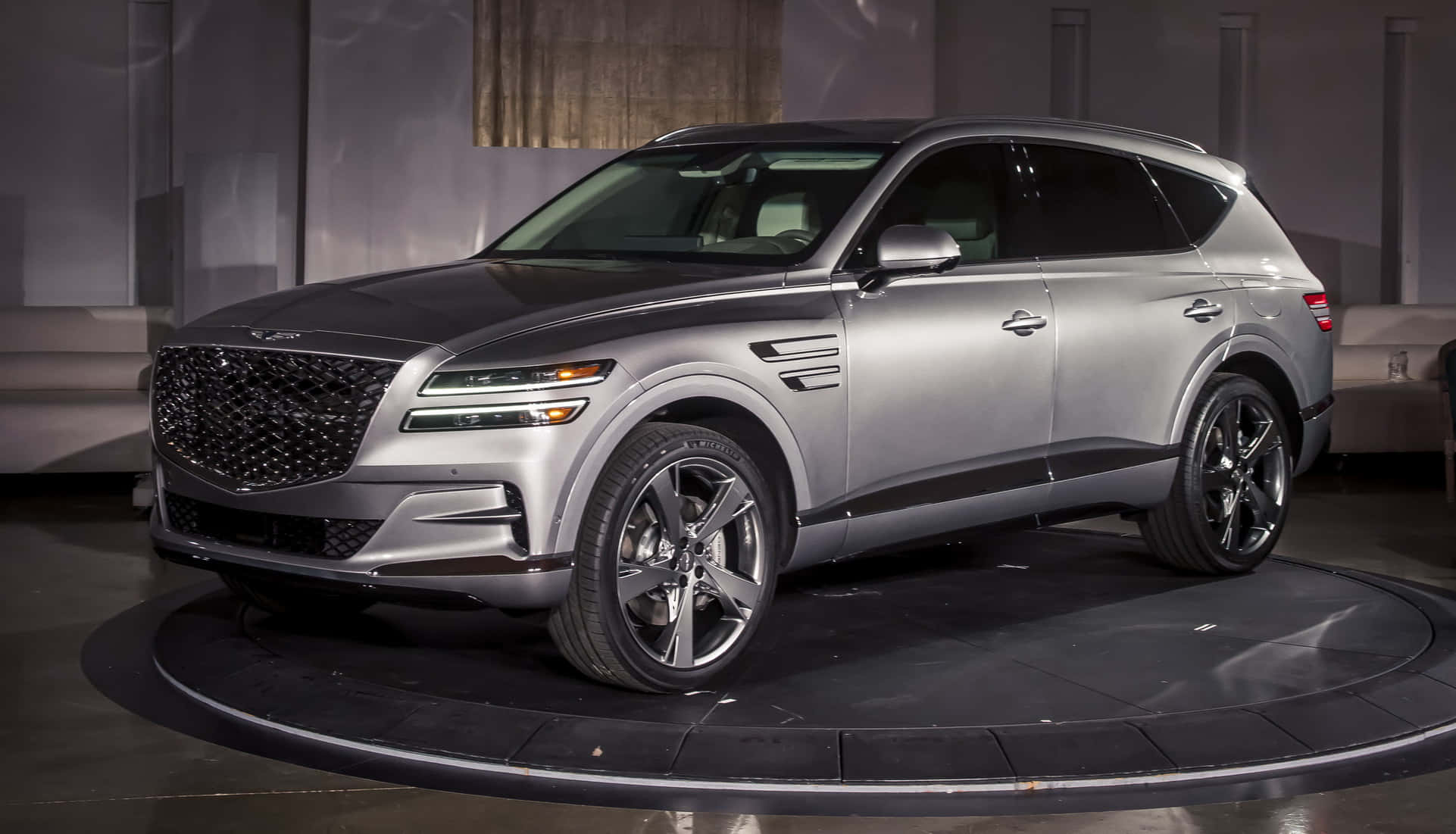 Genesis Gv80 桌布 壁紙 — 一部時尚的銀色 Genesis GV80 SUV 在現代展廳的攝影棚燈光下於旋轉平台上展示。